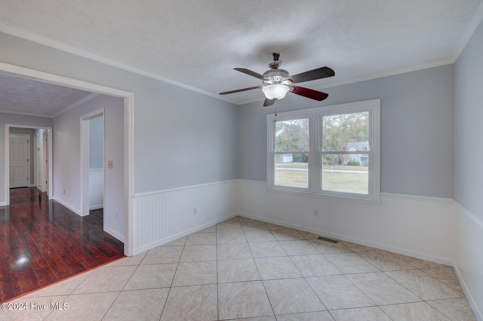 Empty tiled dining area with white wainscoting, a ceiling fan, and two front-facing windows.