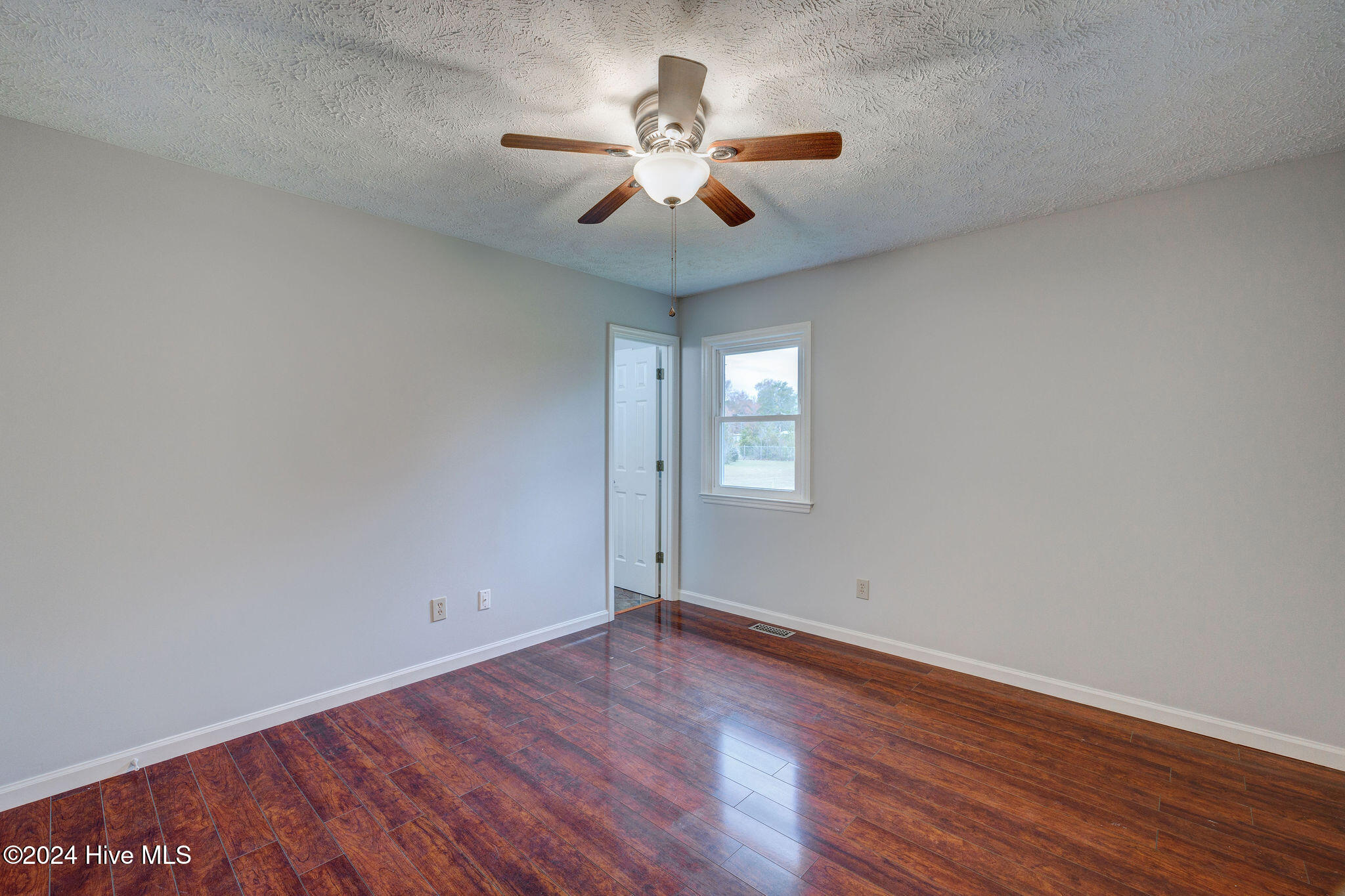 Empty room with reddish wood flooring, pale walls, and a ceiling fan.