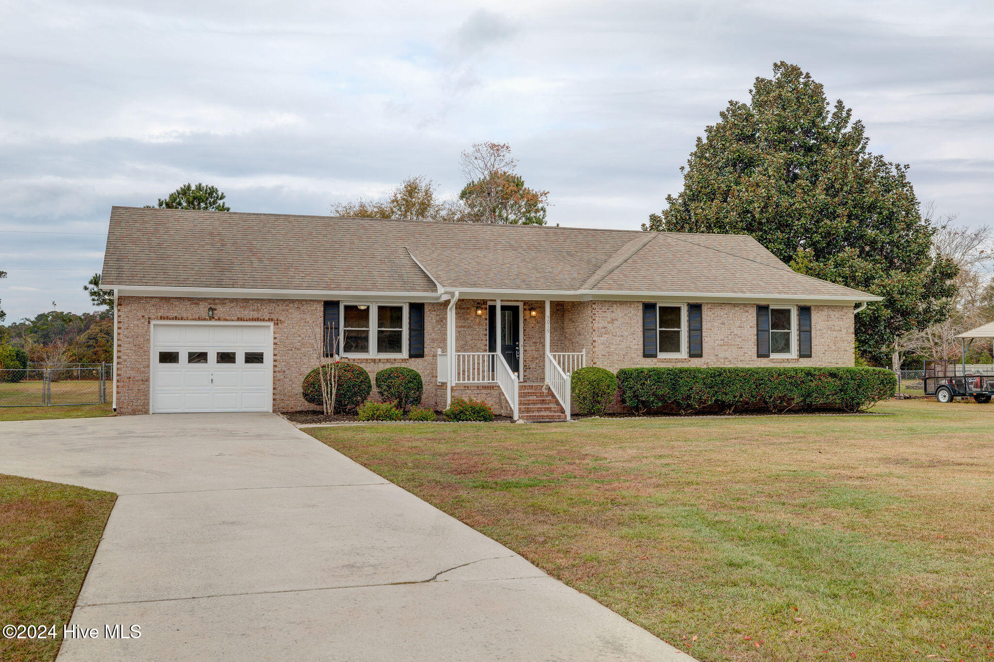 Single-story brick home with an attached garage, white-railed entry steps, trimmed hedges, and a wide driveway.