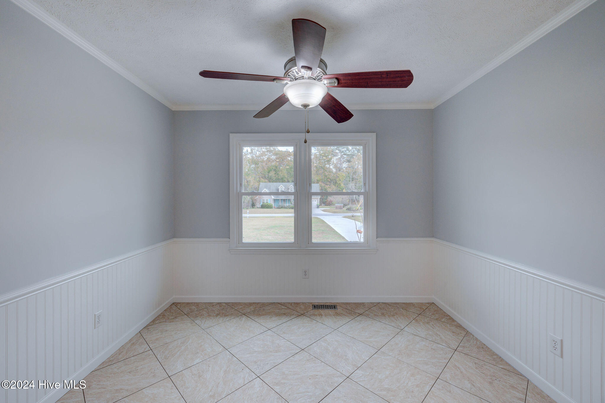 Empty tiled room with white wainscoting, a double window, and a dark wood ceiling fan.