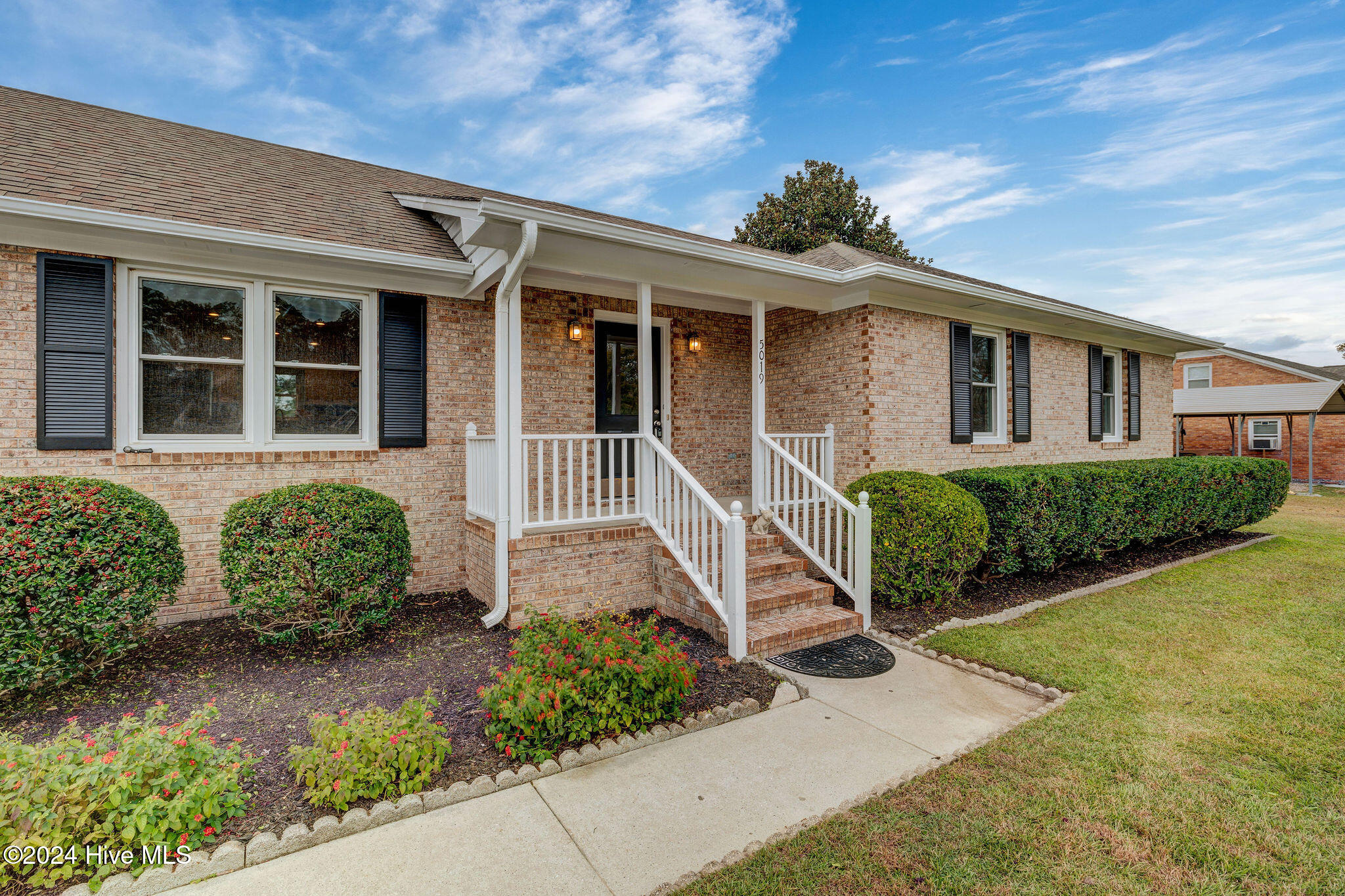 Brick house with a covered front porch, white railings, and landscaped flower beds.