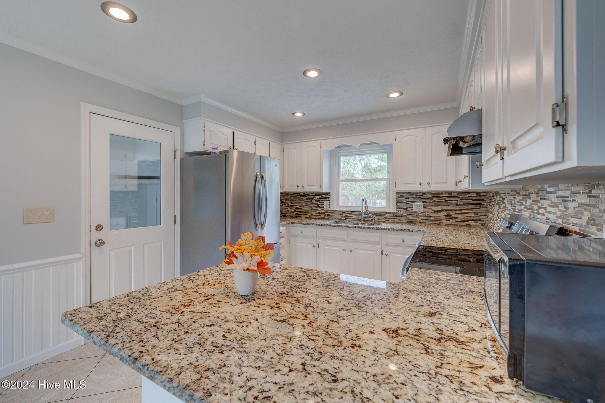 Kitchen with white cabinets, stainless steel appliances, and a broad granite peninsula.