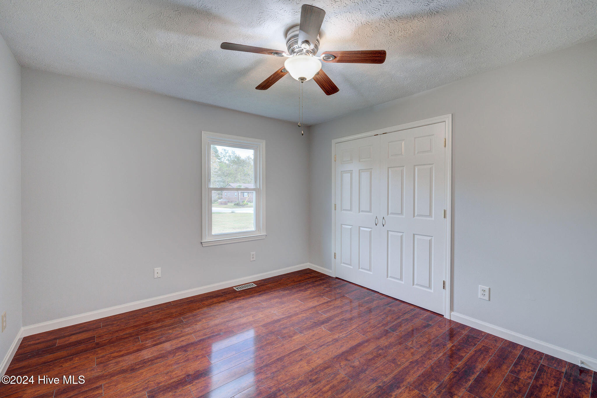 Empty bedroom with hardwood floors, a ceiling fan, and white double closet doors.