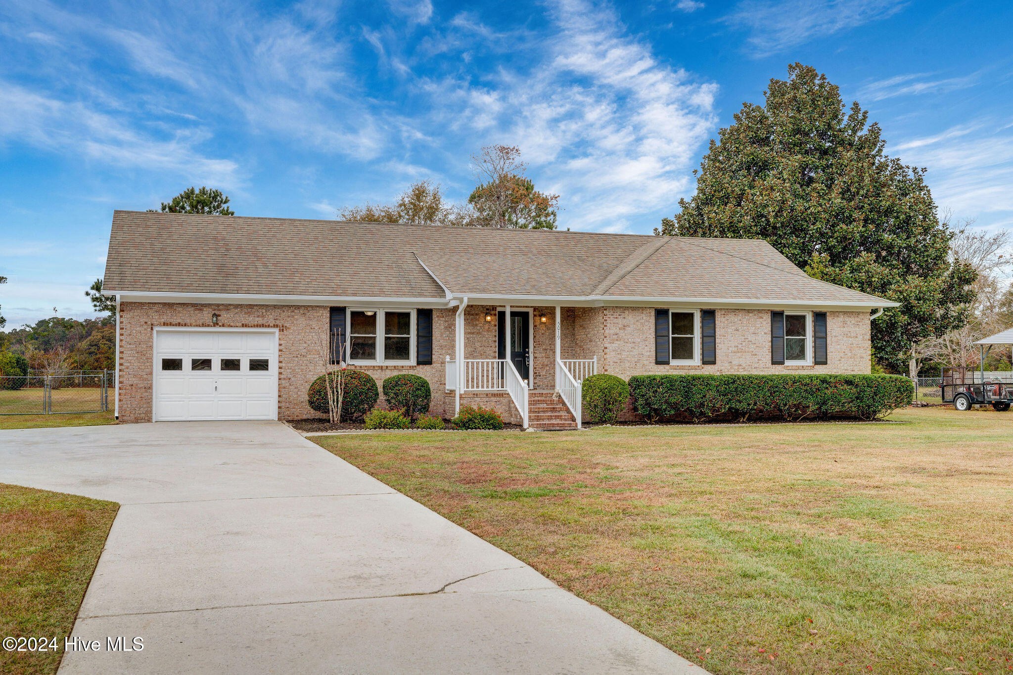 Single-story brick home with an attached garage, broad driveway, and white-railed front steps.
