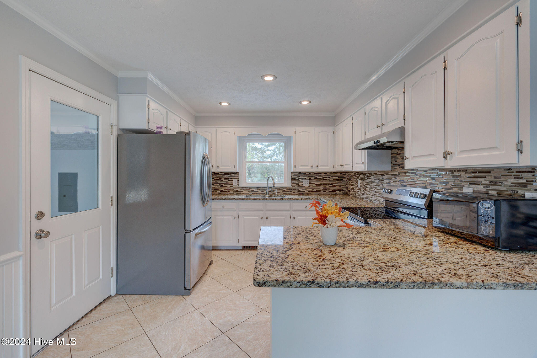 Kitchen with white cabinets, stainless steel appliances, mosaic backsplash, and a granite-topped island.