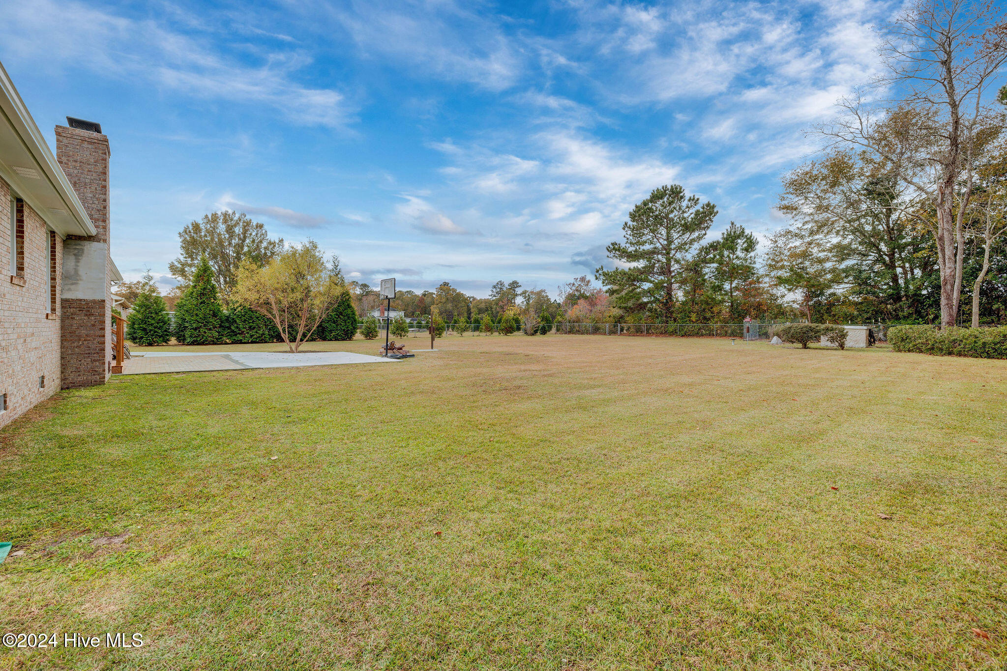 Backyard with a broad lawn, basketball hoop, paved patio, and chain-link fence.