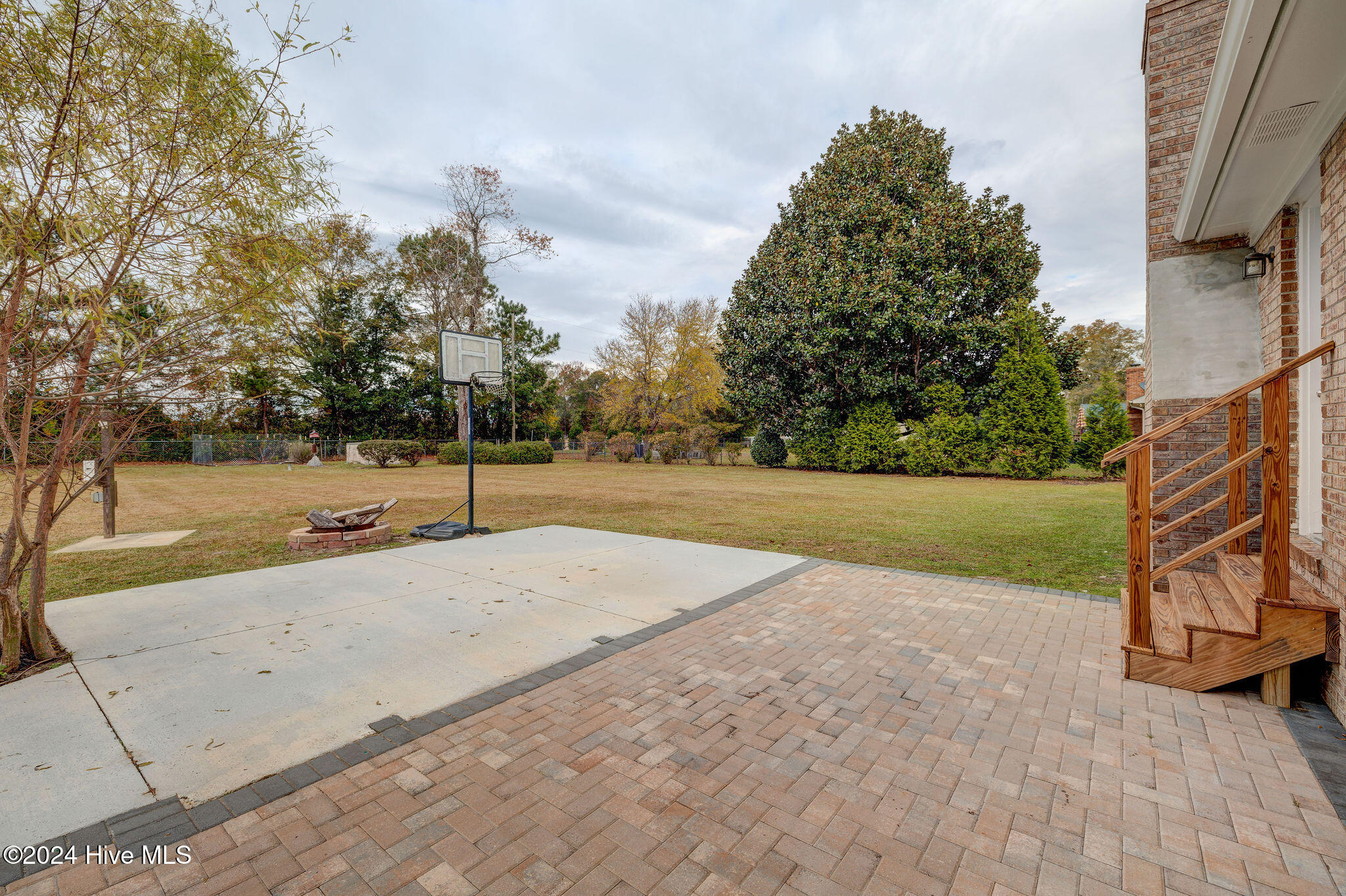Backyard patio and basketball court with a portable hoop, brick fire pit, and wooden steps.