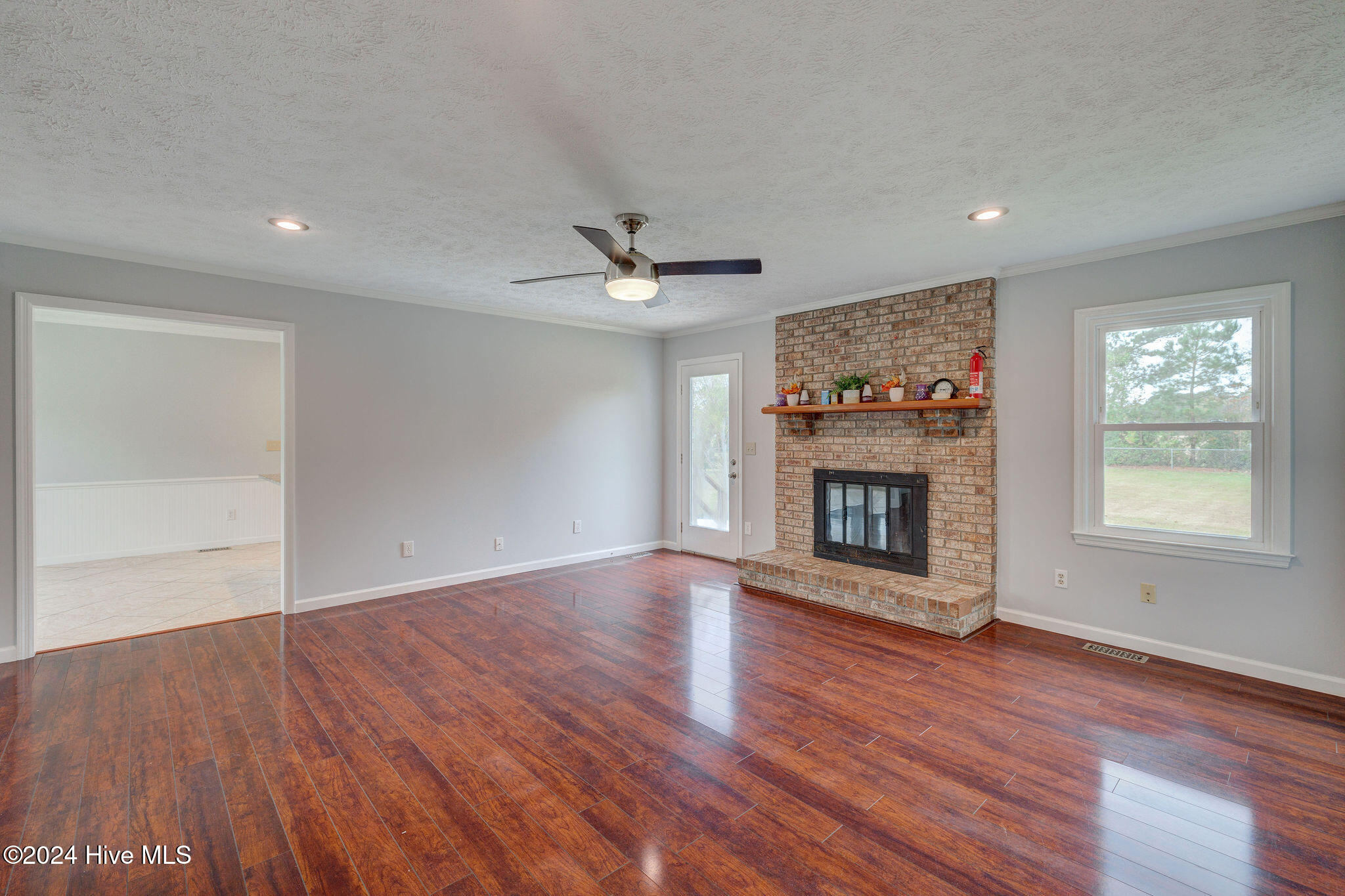 Living room with hardwood floors, a brick fireplace, and a window overlooking the yard.