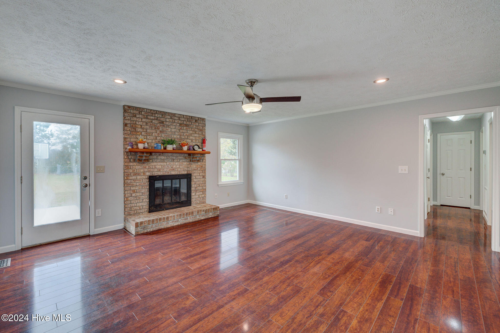 Empty living room with brick fireplace, raised hearth, and glossy hardwood floors.
