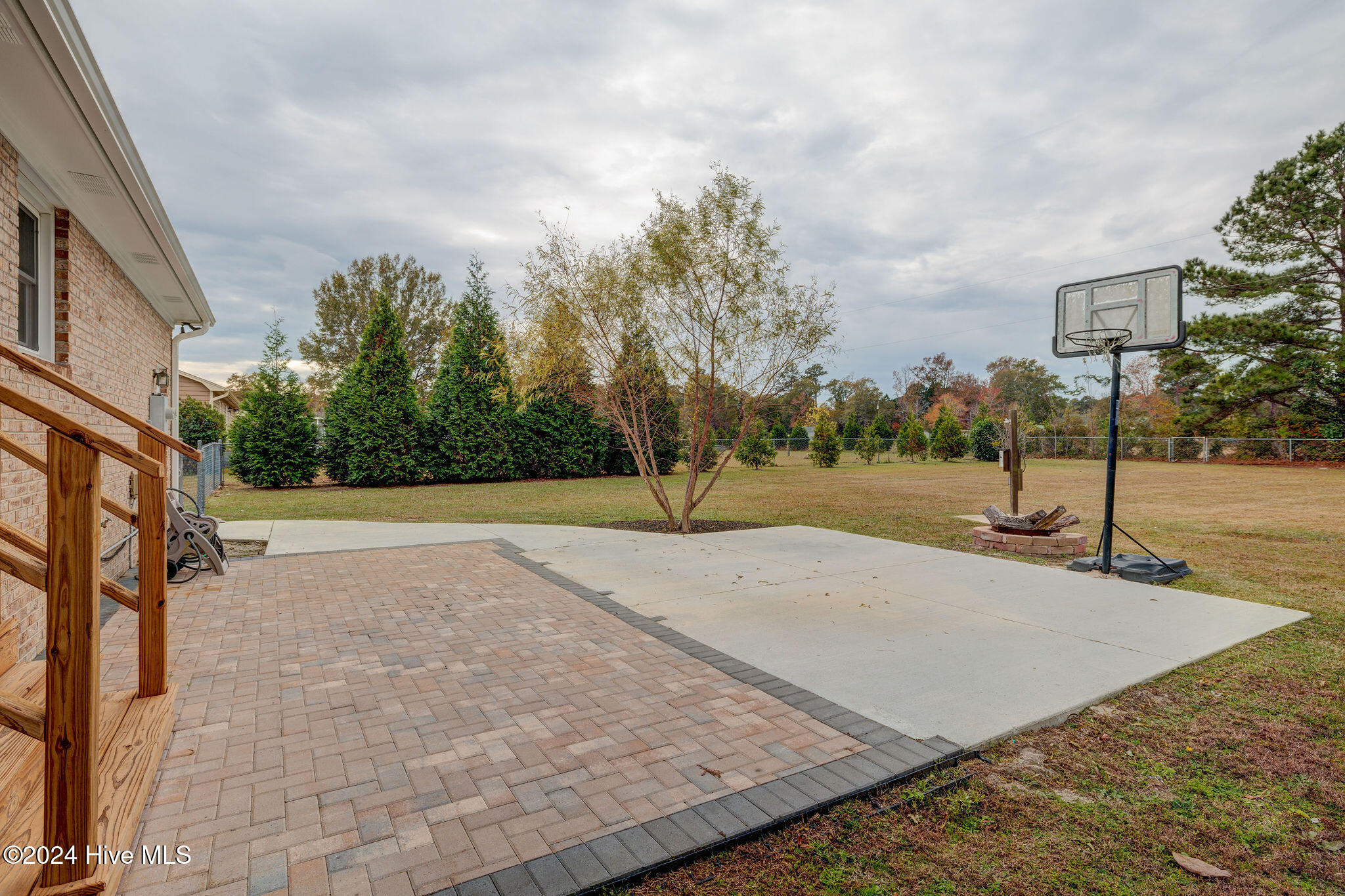 Backyard patio with brick pavers, a basketball hoop, and a fire pit beside a broad lawn.