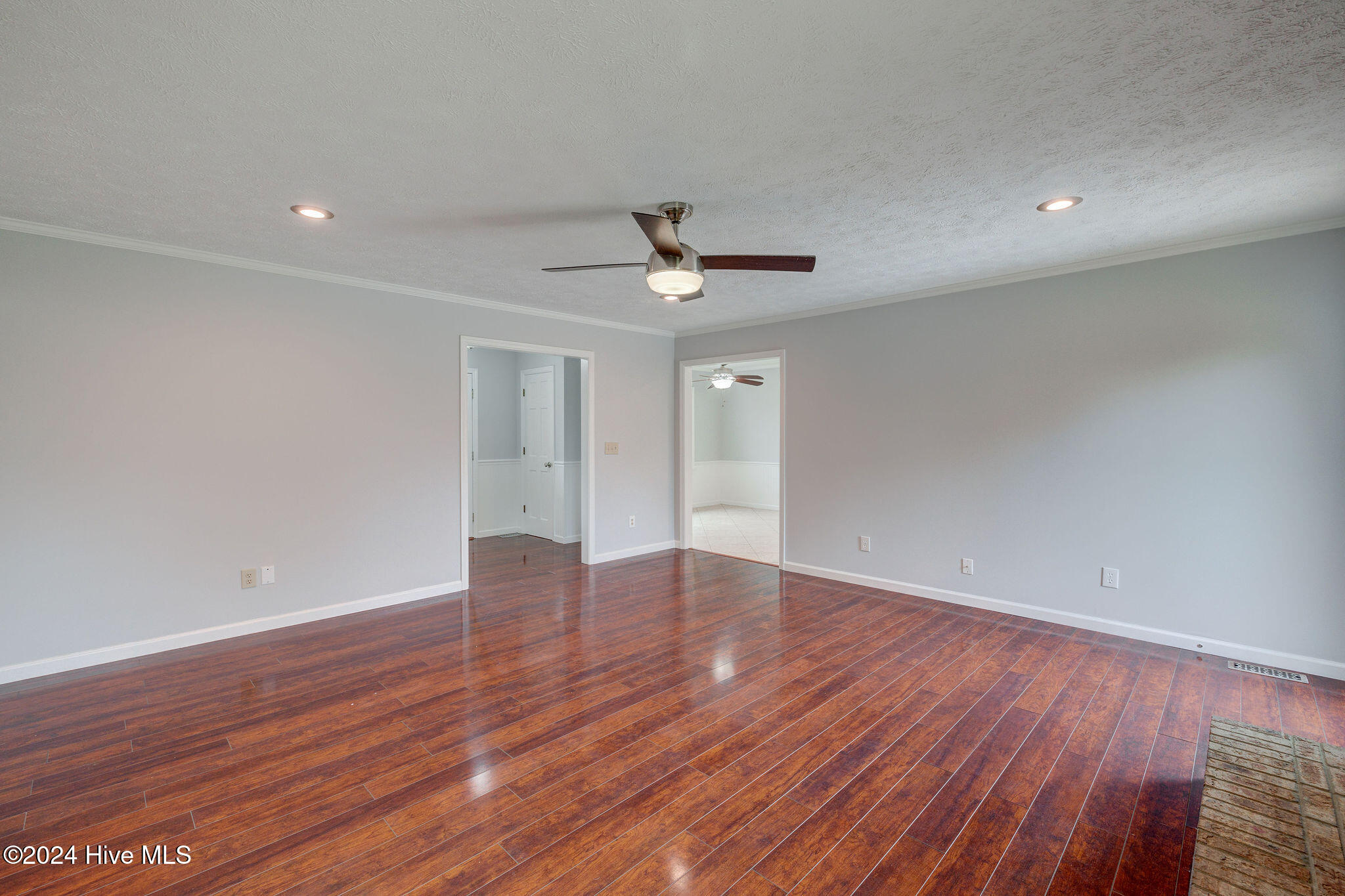 Vacant living room with reddish-brown wood flooring, gray walls, and a ceiling fan.