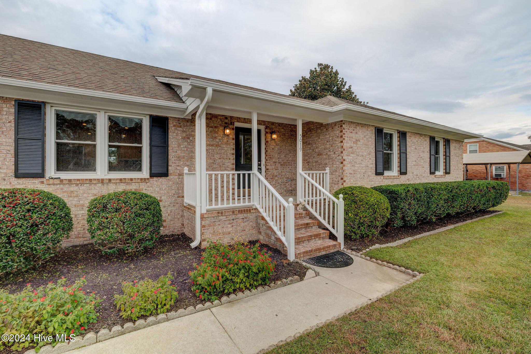 Brick house with a covered porch, white railings, brick steps, and landscaped front beds.