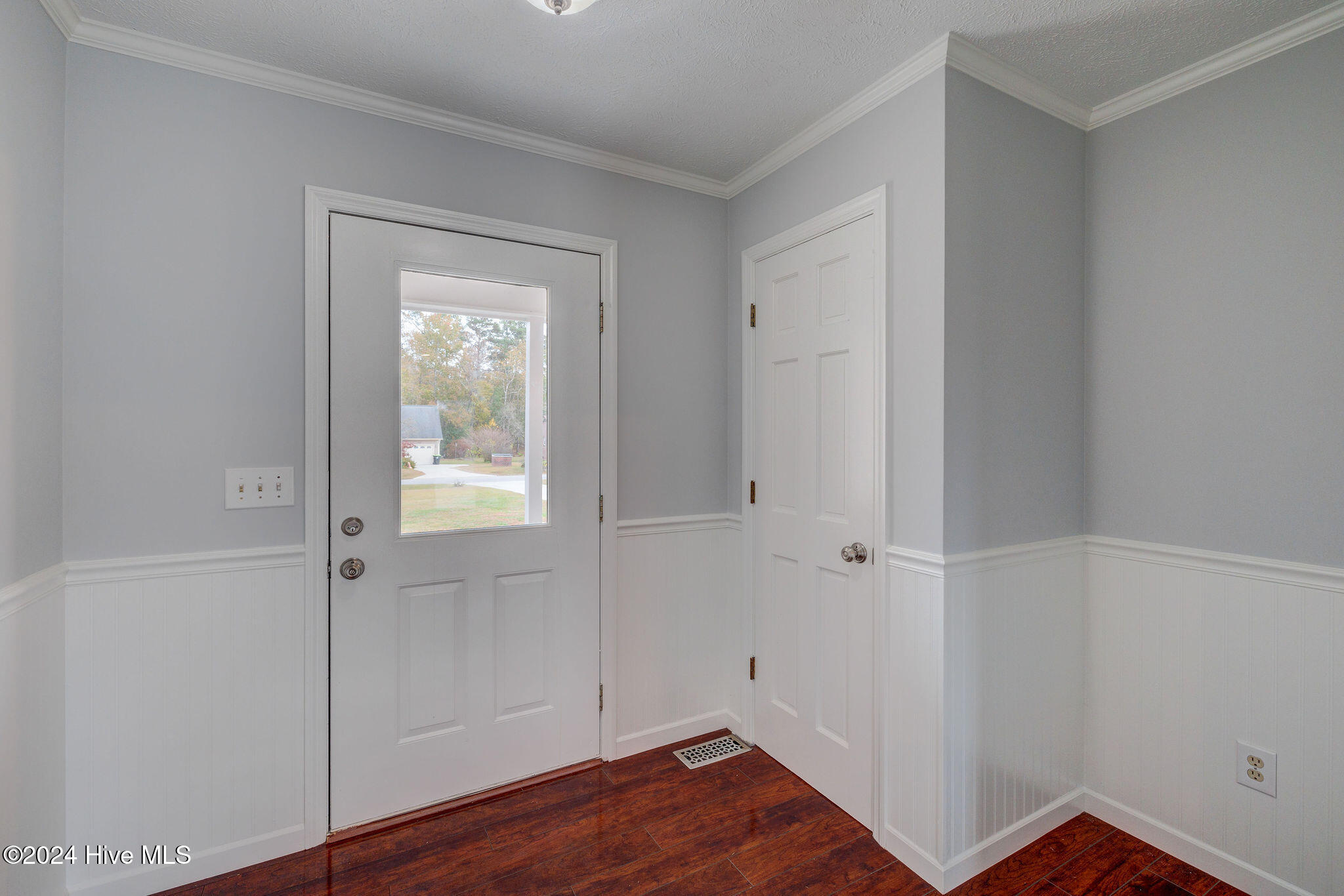 Entryway with a windowed front door, white wainscoting, and dark wood flooring.