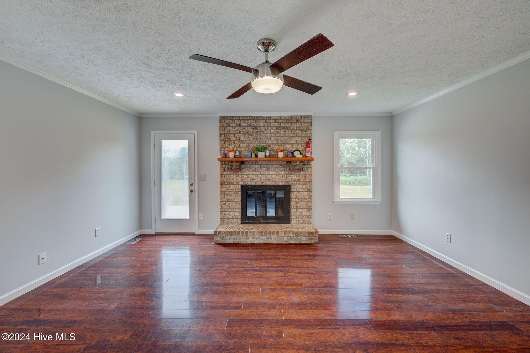 Unfurnished living room with a brick fireplace, raised hearth, and dark reddish plank flooring.