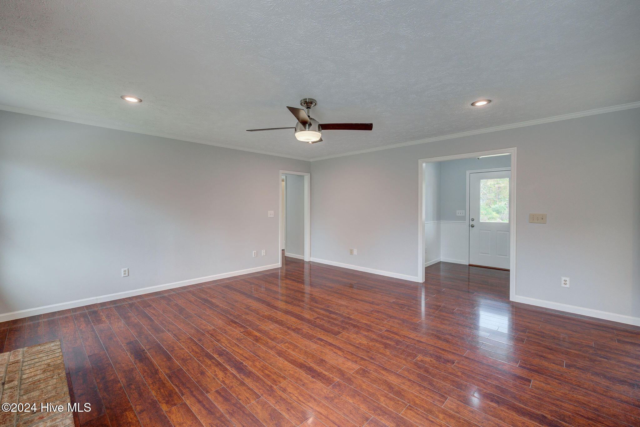 Empty room with glossy reddish-brown floors, a ceiling fan, and an entryway with a glass-panel door.