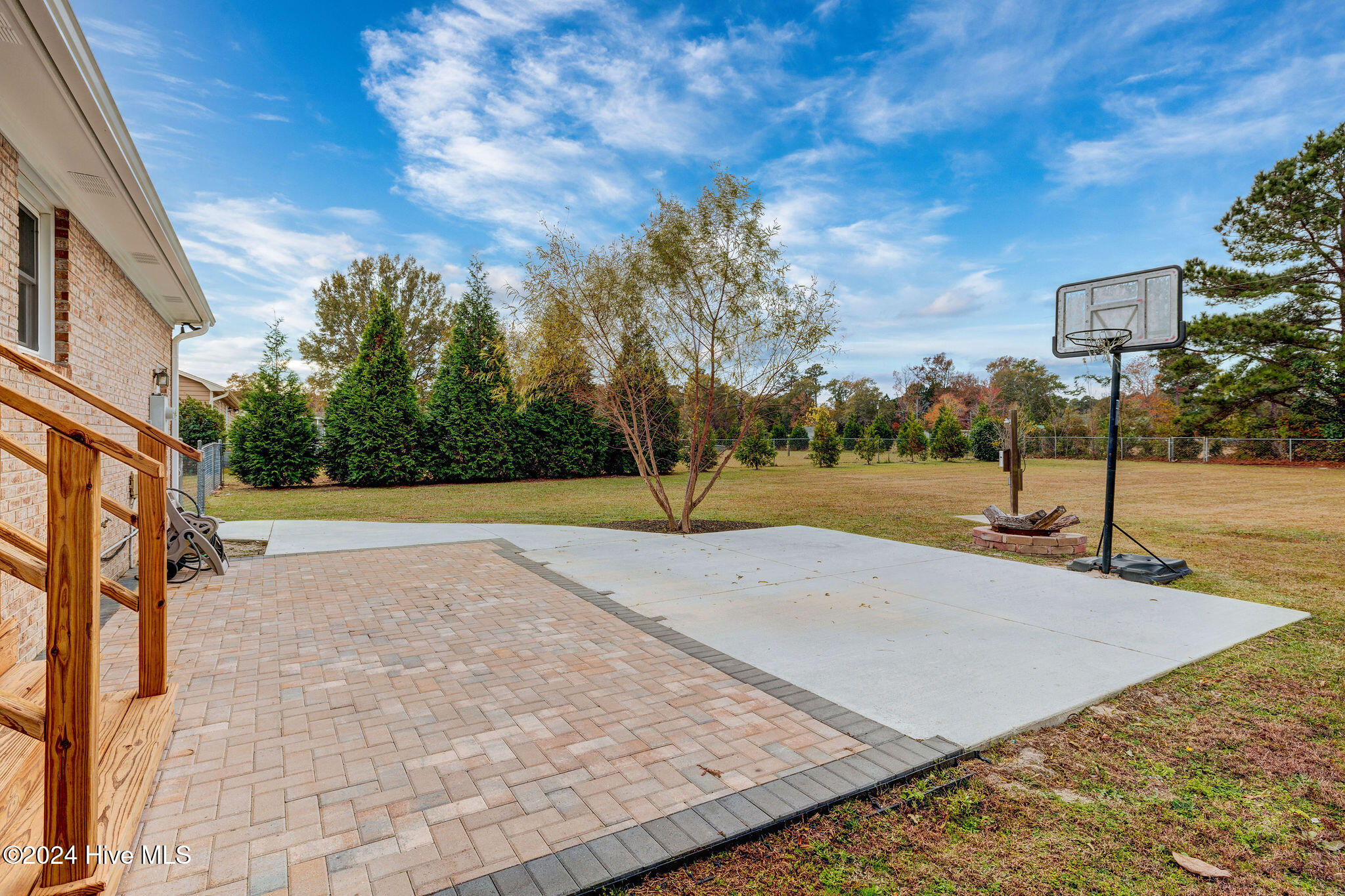 Backyard patio with brick pavers, a concrete basketball area, fire pit, and fenced lawn.