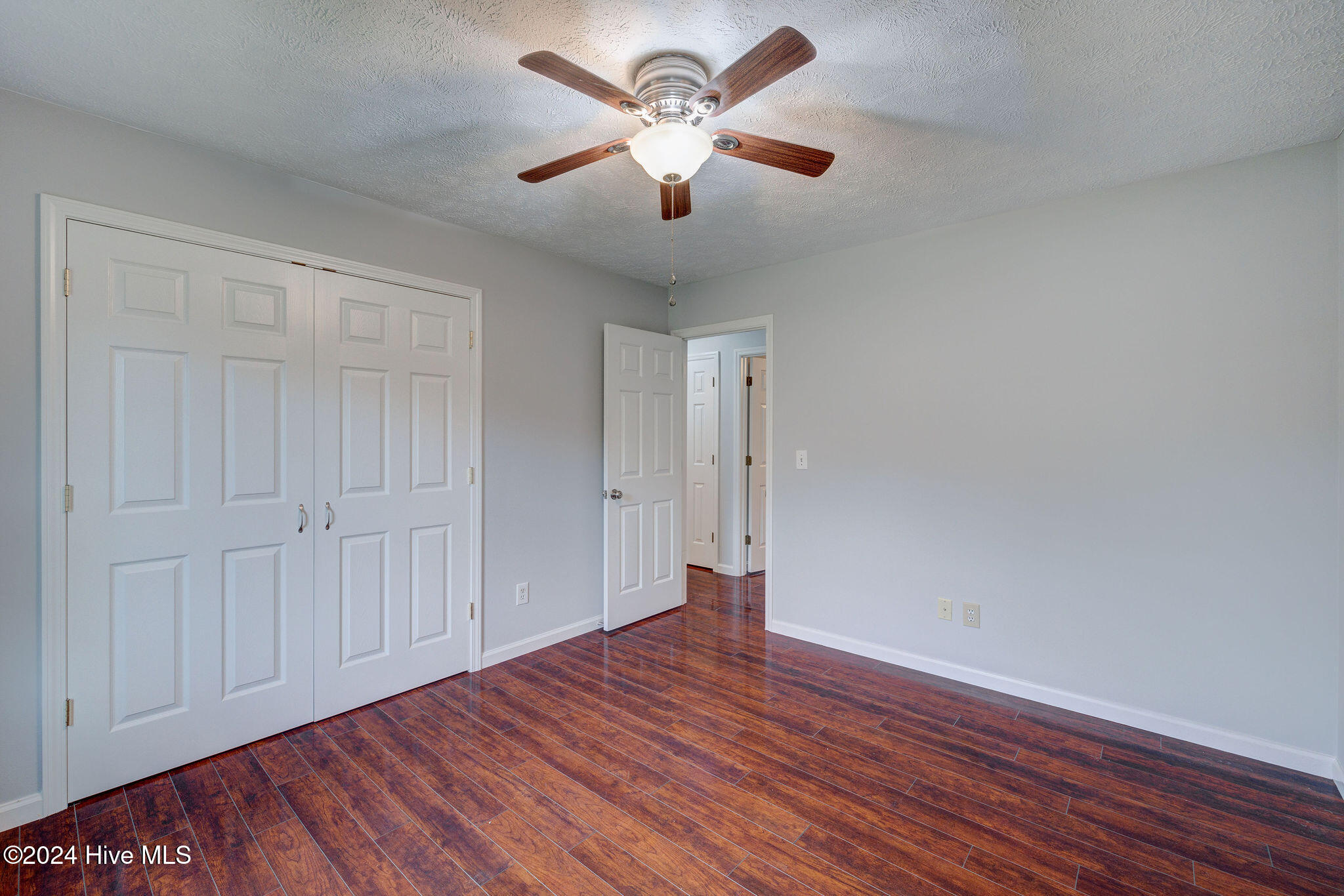 Empty bedroom with wood-look flooring, double closet doors, and a ceiling fan with light.