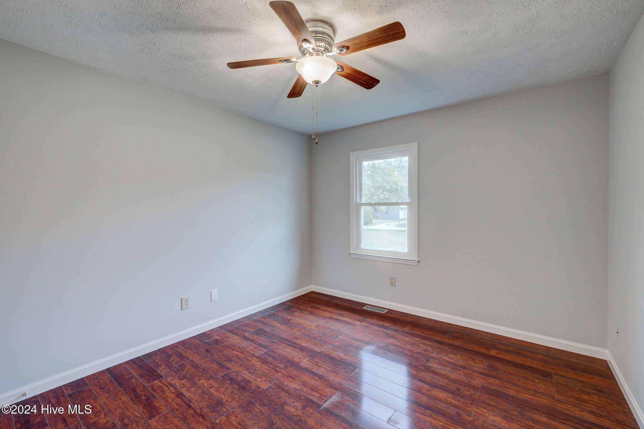 Empty bedroom with dark wood flooring, gray walls, and a ceiling fan.