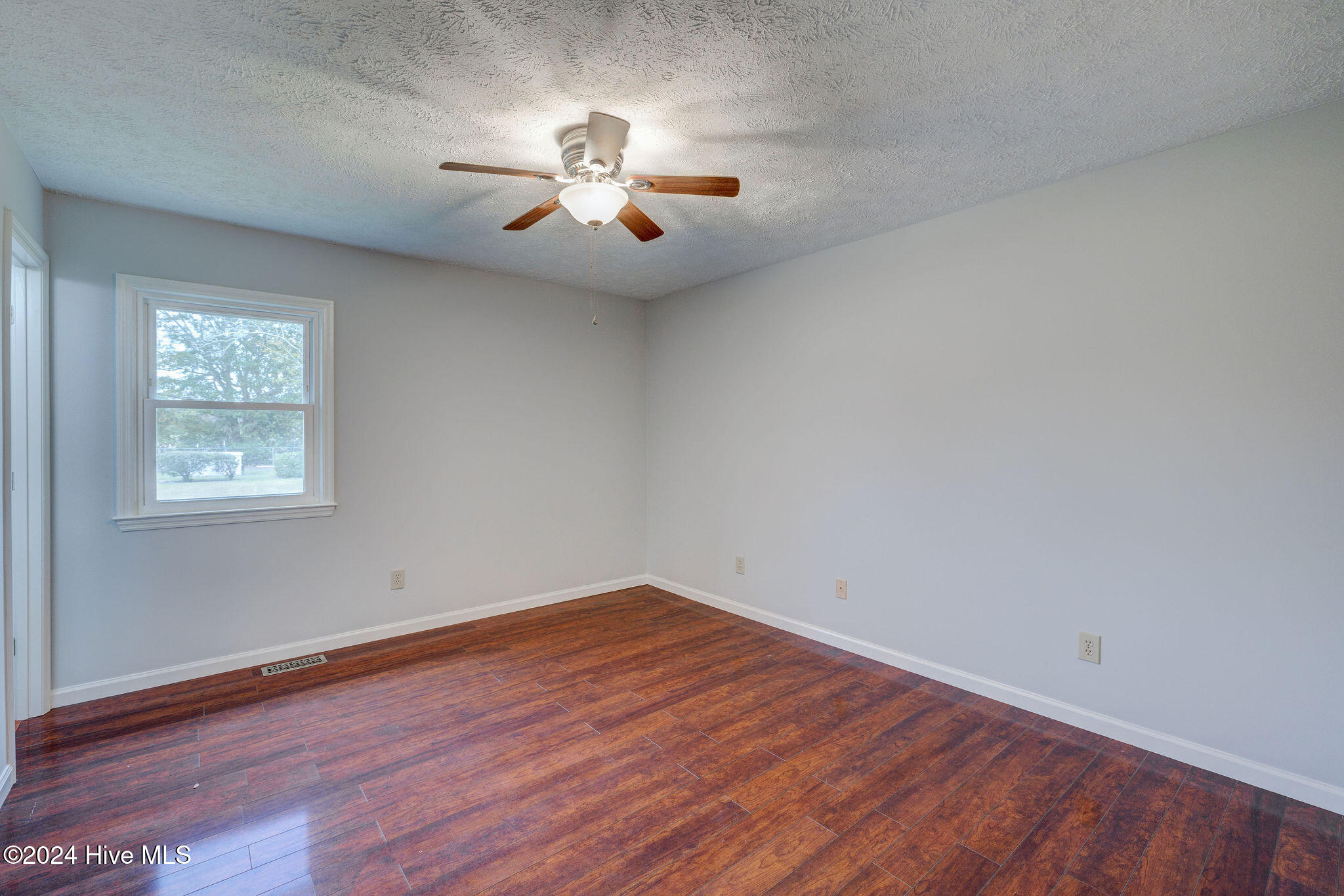 Empty room with hardwood floors, a window, and a ceiling fan with light.