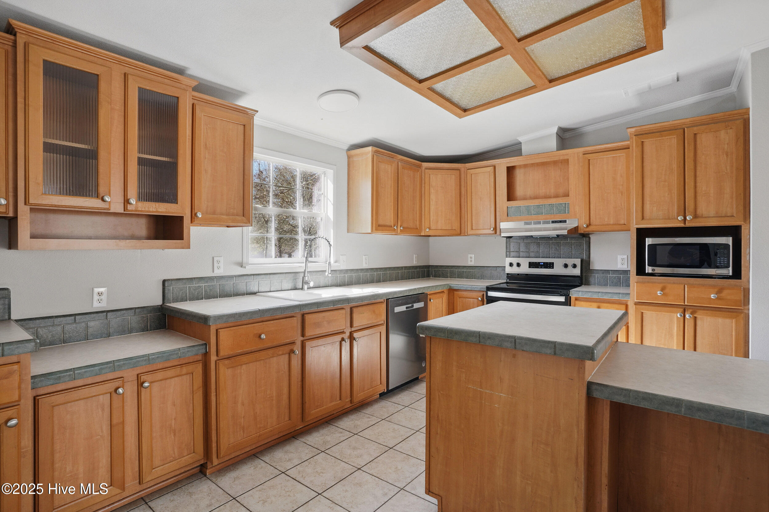 Kitchen with honey-toned cabinets, gray tile counters, a central island, and a window above the sink.
