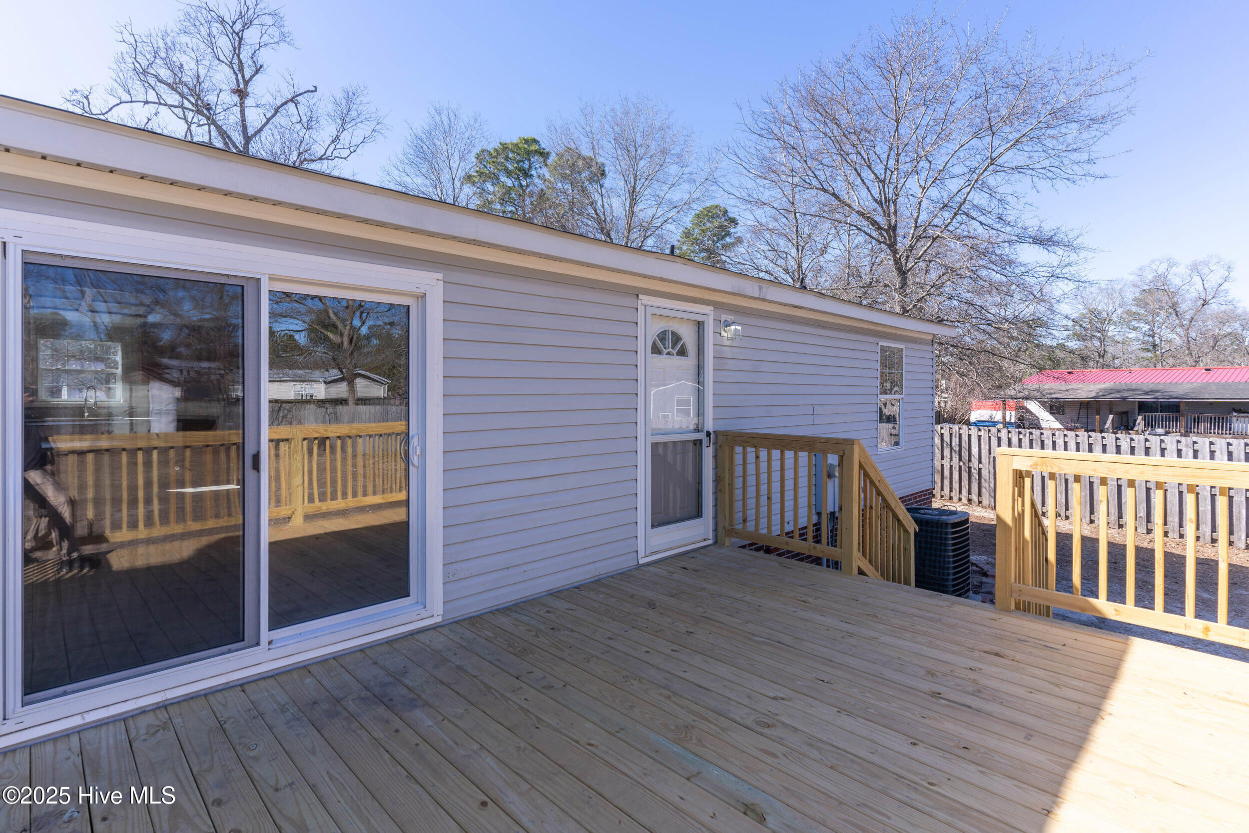 Wooden deck beside a light-colored home, with sliding glass doors and wooden railings.