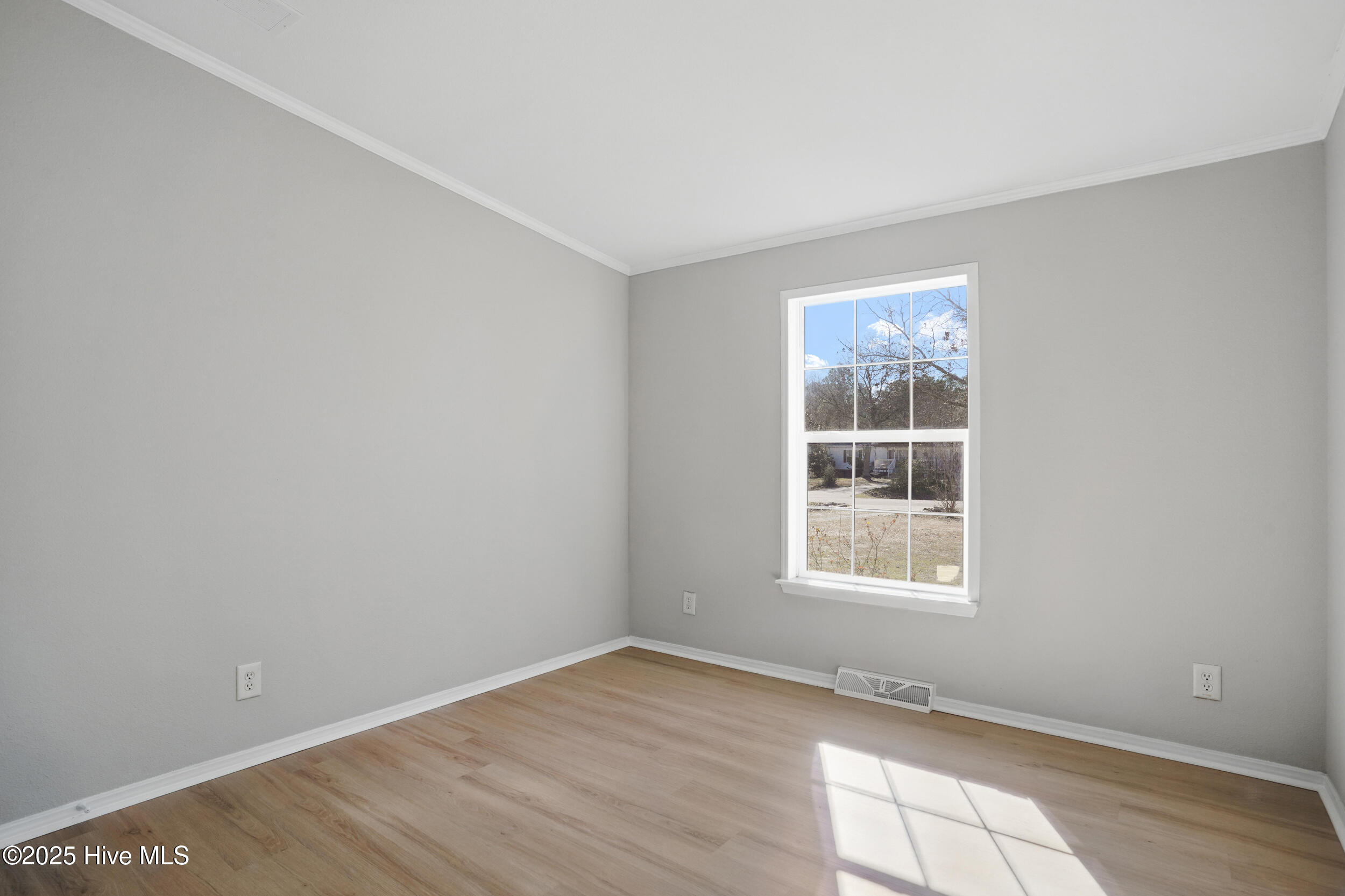 Empty room with gray walls and pale wood floors, lit by sunlight through a large window.