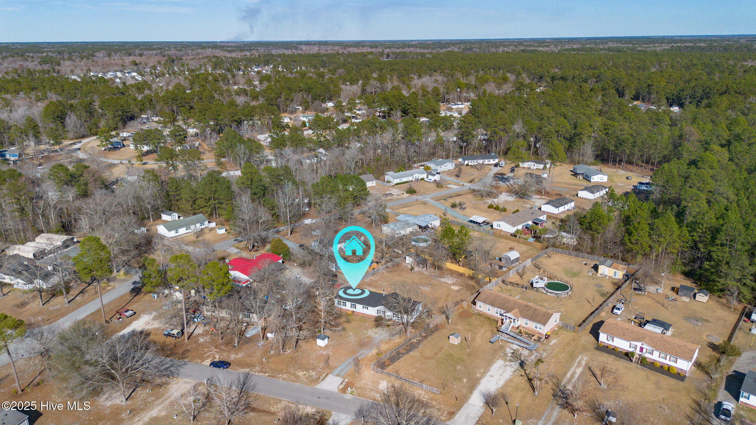 Aerial view of the marked home among neighborhood houses and surrounding woodland.