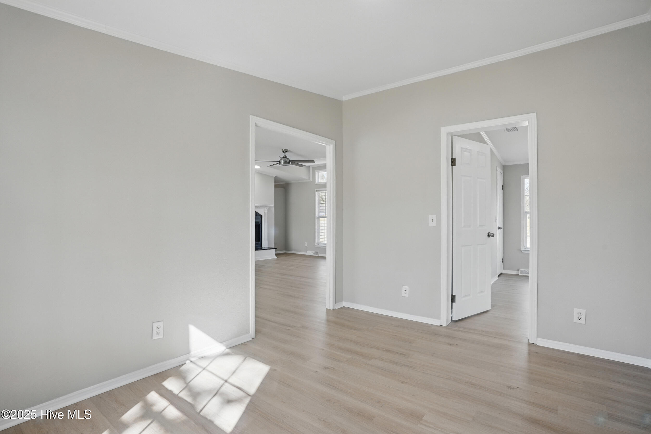 Empty room with light flooring and sunlight, looking through doorways into adjoining rooms.