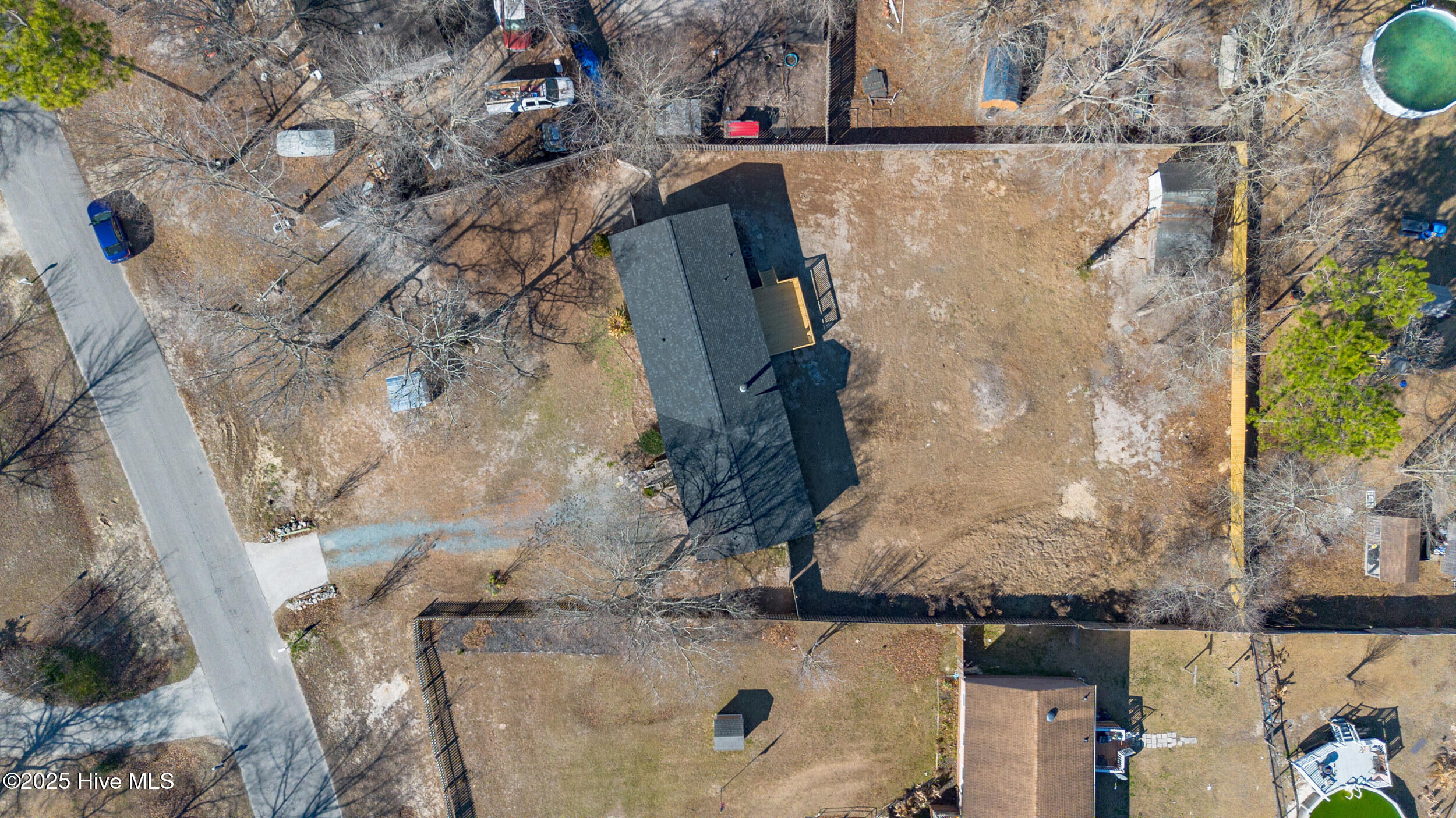 Aerial view of a dark-roofed house with a large fenced, mostly bare backyard.