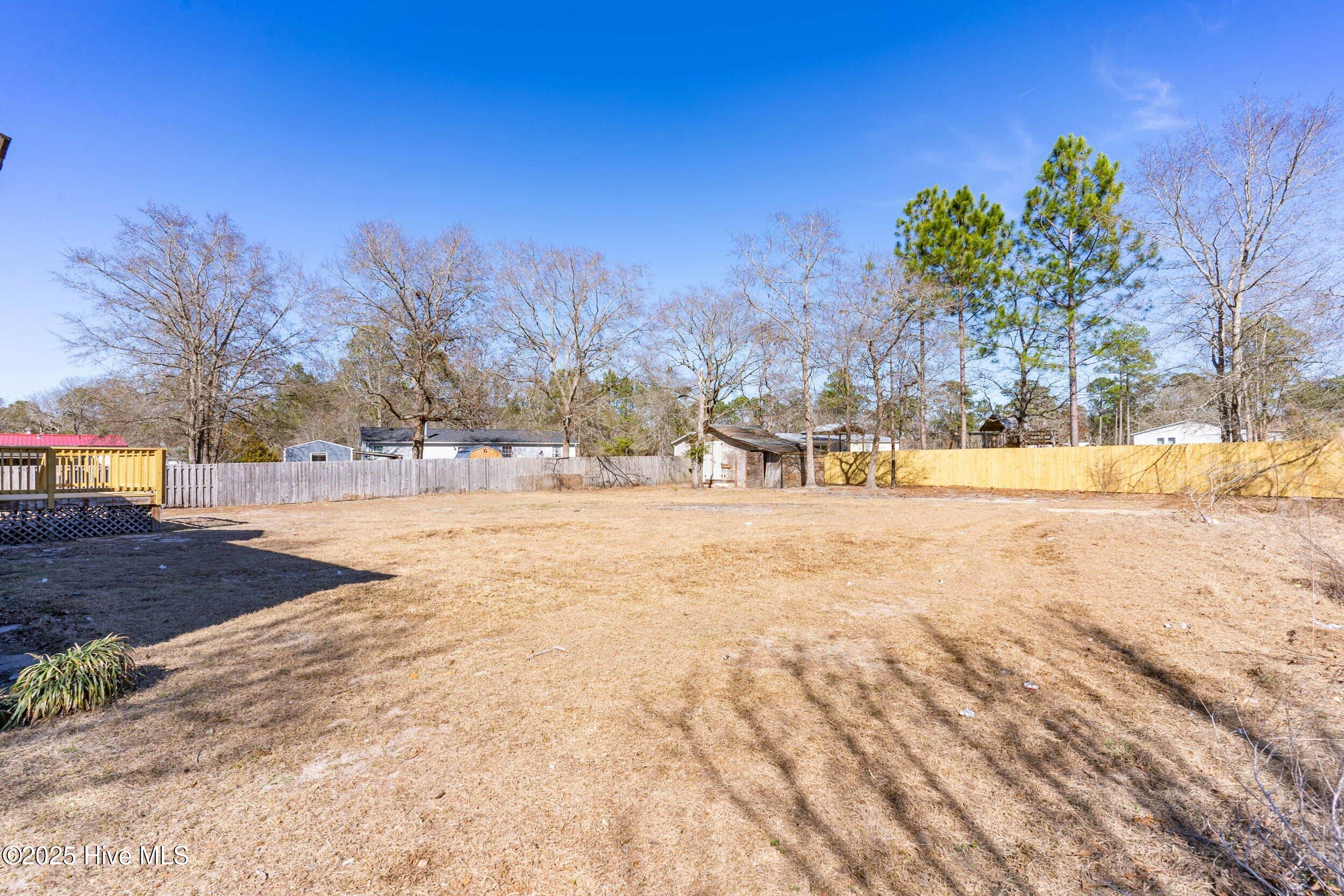 Backyard with a wooden deck, fenced yard, and leafless trees.