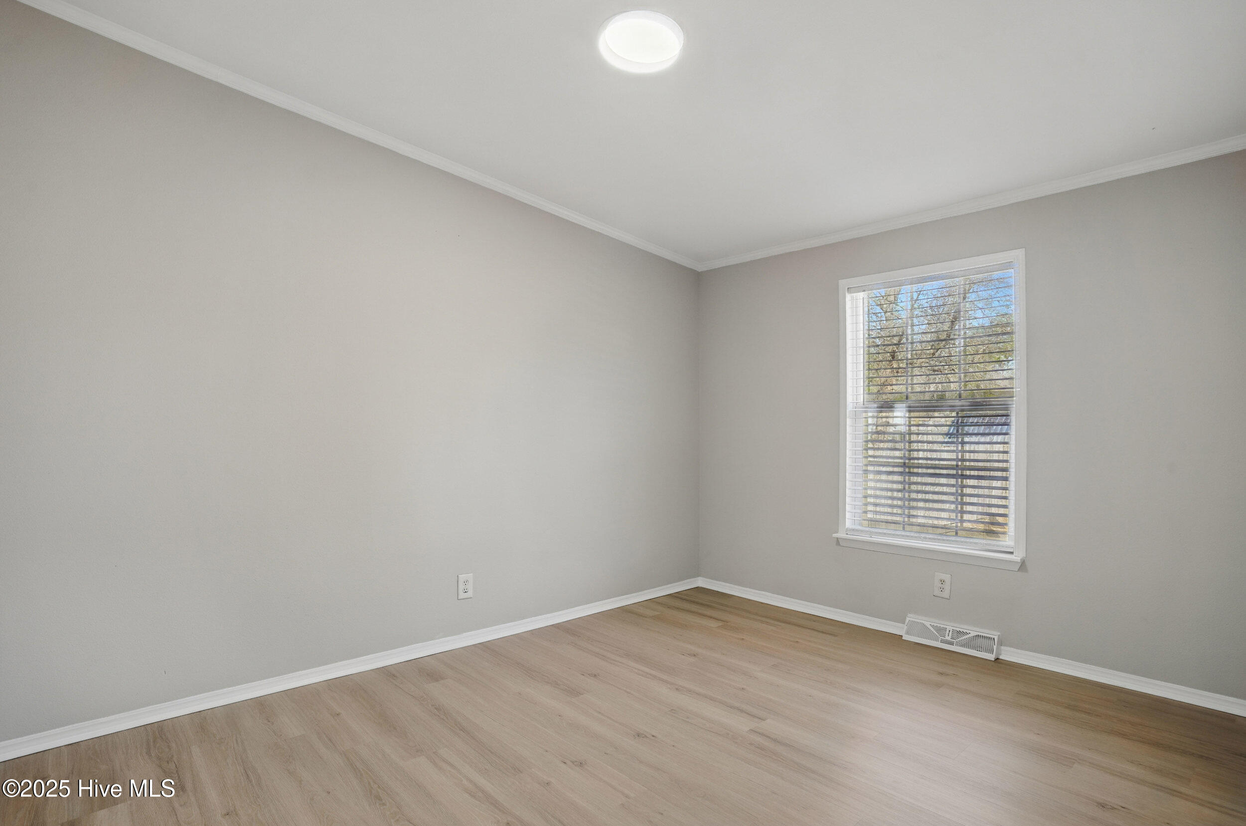 Empty room with light wood flooring, pale gray walls, and a window with white blinds.