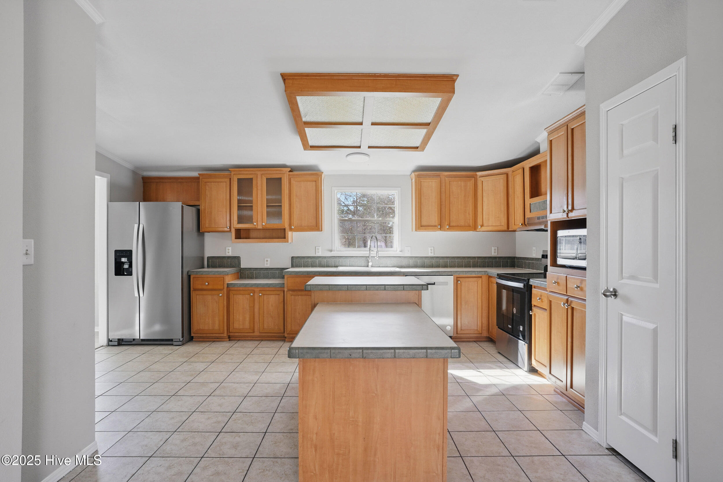 Kitchen with warm wood cabinets, a large central island, stainless steel appliances, and a window above the sink.