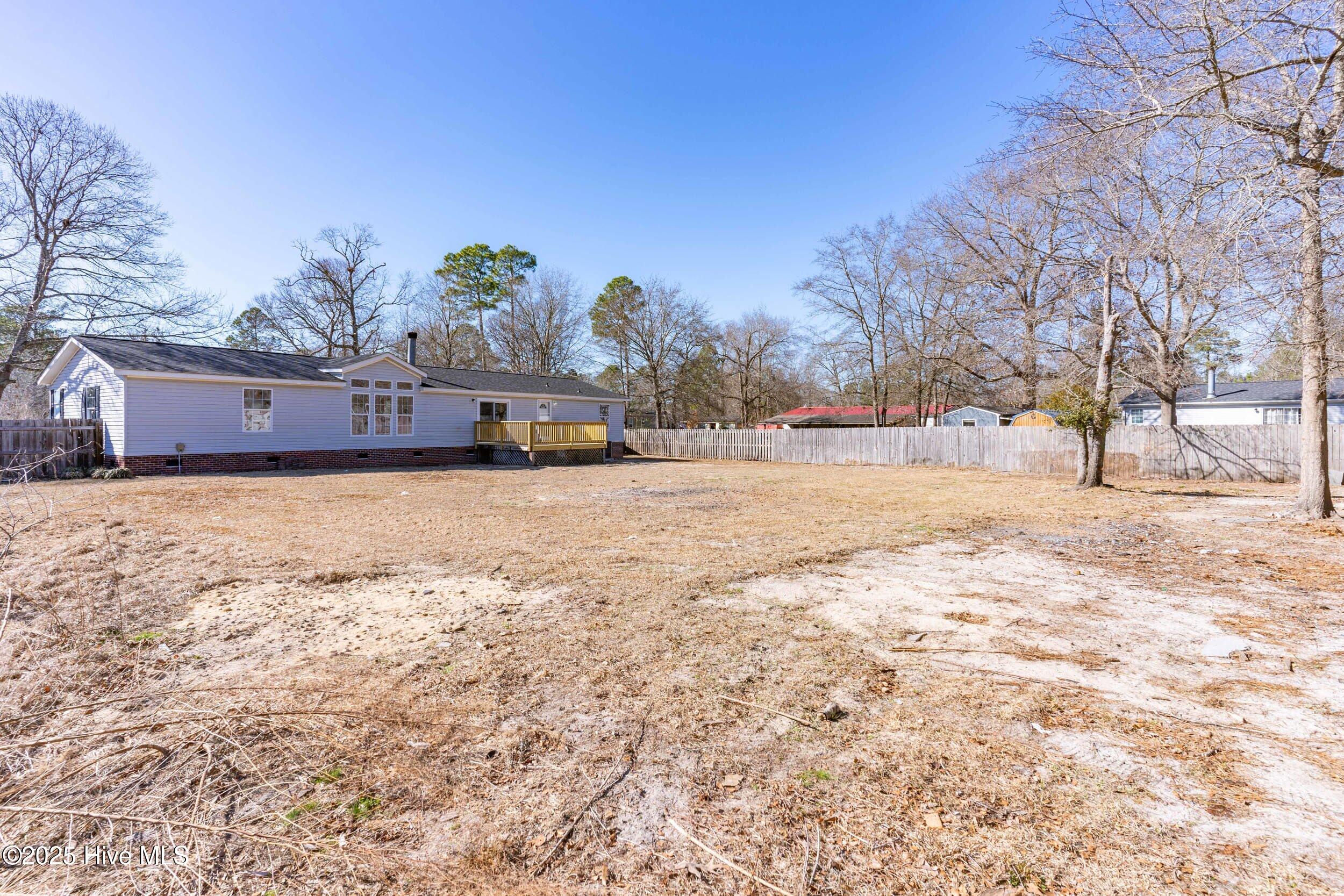Single-story home with a small deck overlooking a broad fenced yard and leafless trees.