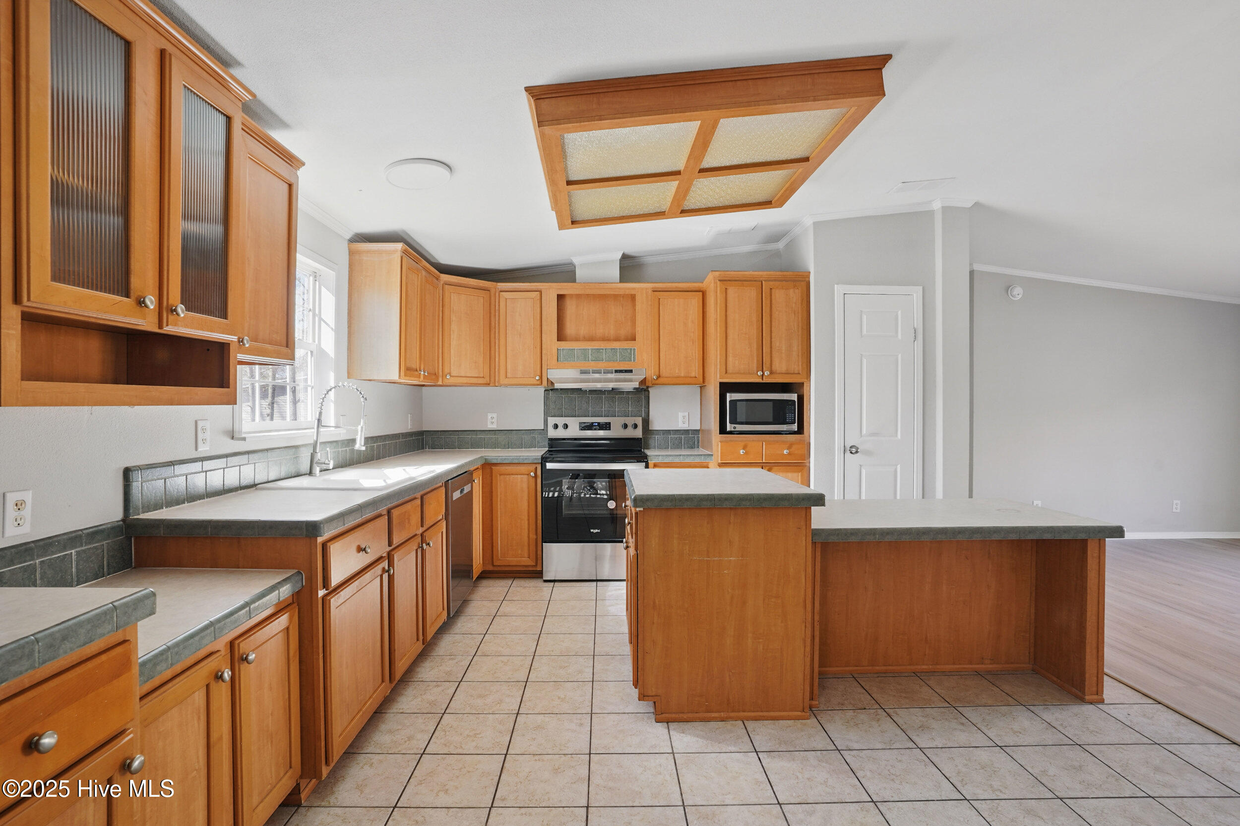 Vacant kitchen with honey-colored cabinets, gray tile counters, a central island, and stainless steel range.