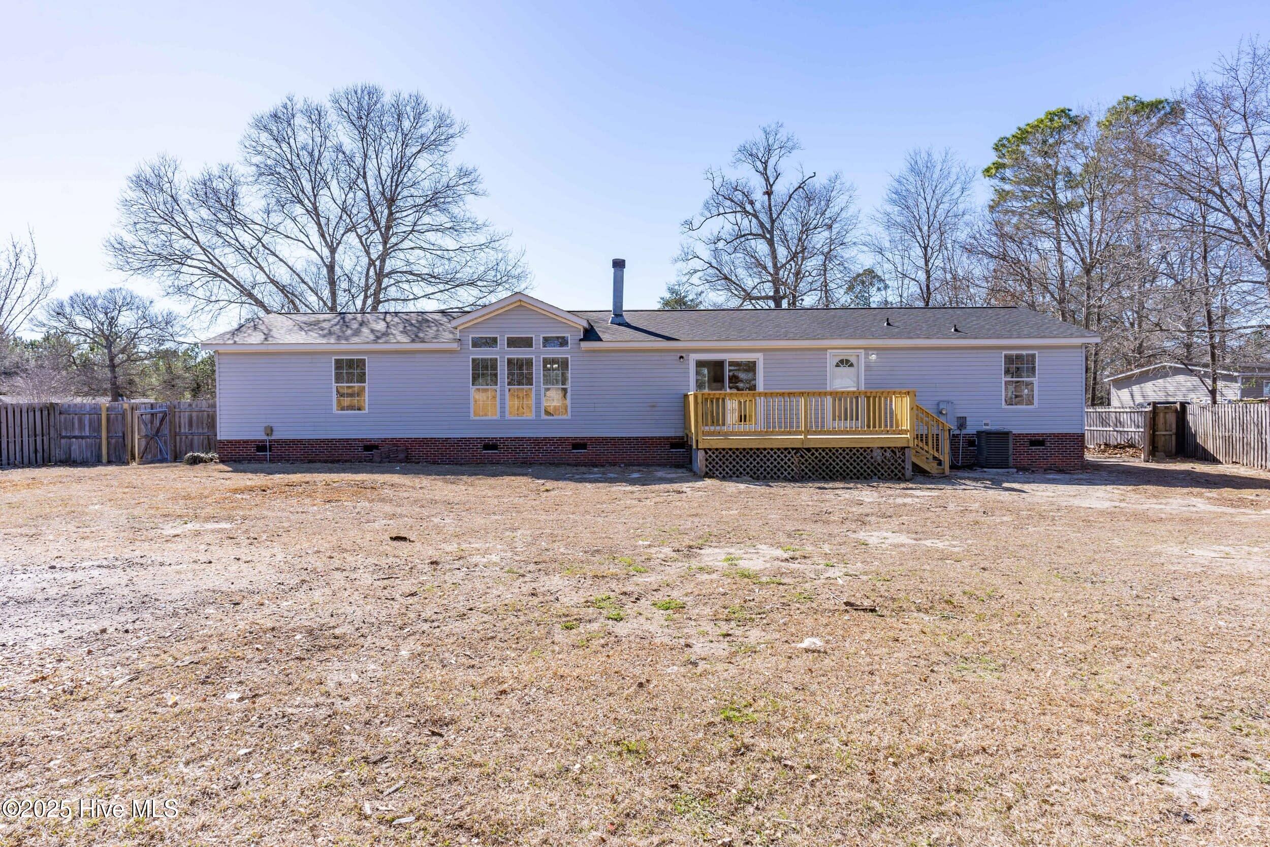 Rear of a single-story home with a raised wooden deck, broad dry yard, and leafless trees.