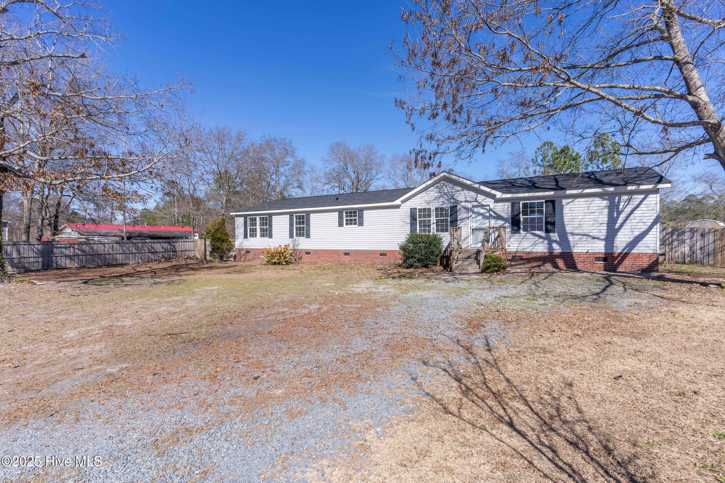 Single-story white house with brick foundation, small entry deck, and gravel driveway.