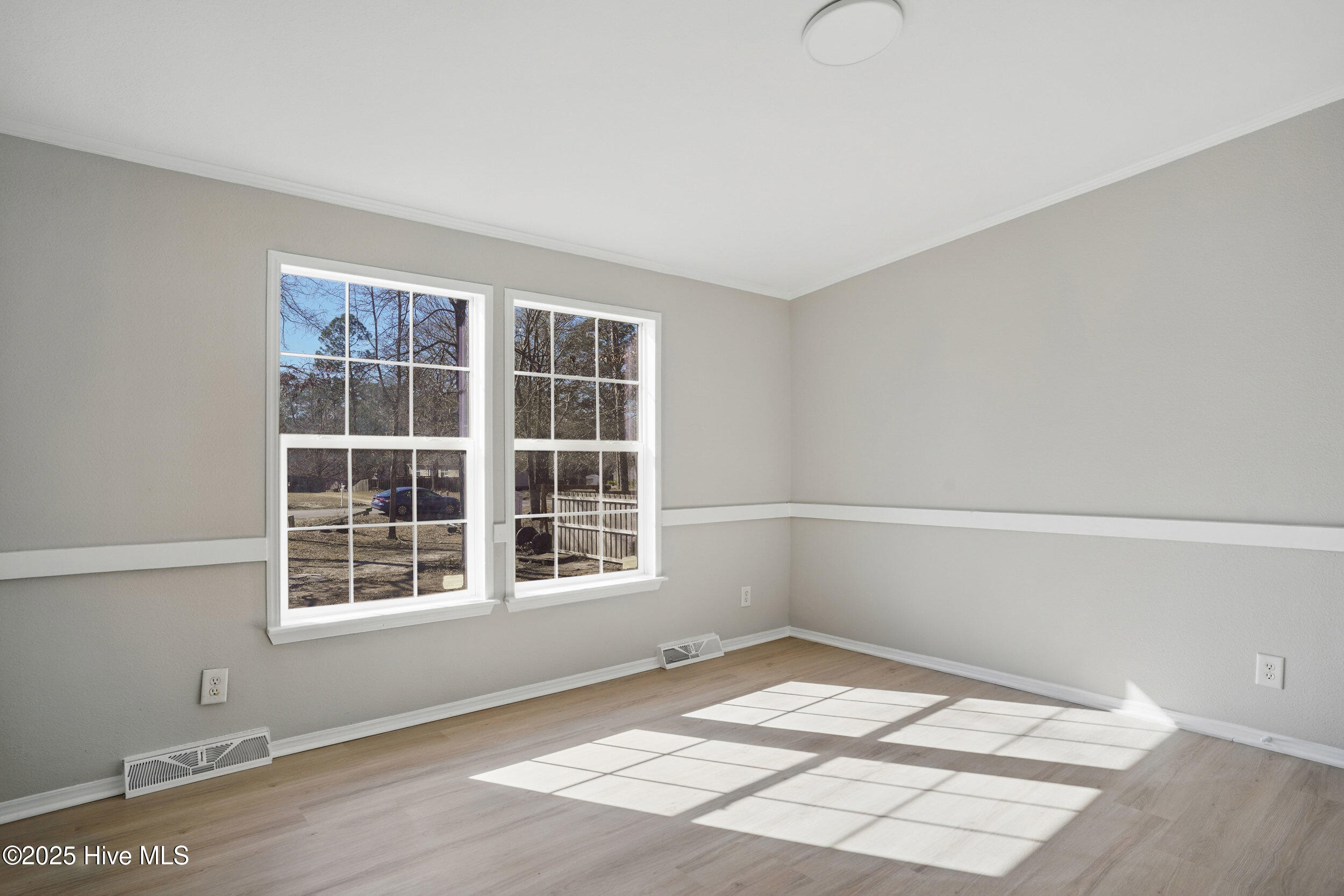 Empty room with light wood floors and two large windows casting sunlight across the floor.