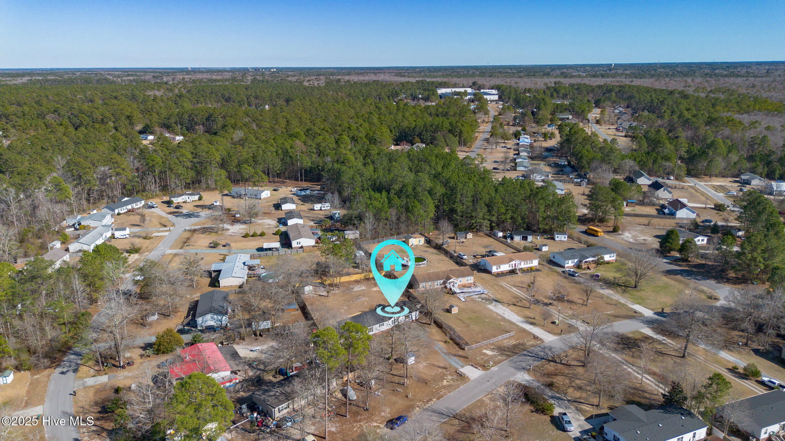 Aerial view of the property in a wooded residential neighborhood, marked with a turquoise location pin.