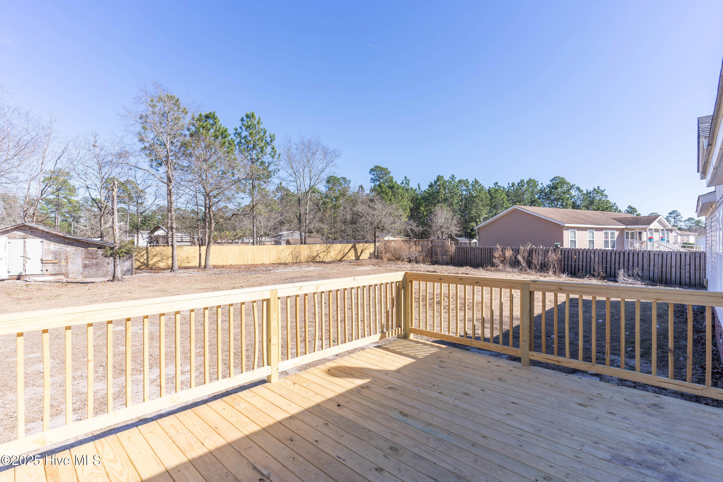 Wooden deck overlooking a fenced backyard with a shed and bare trees.