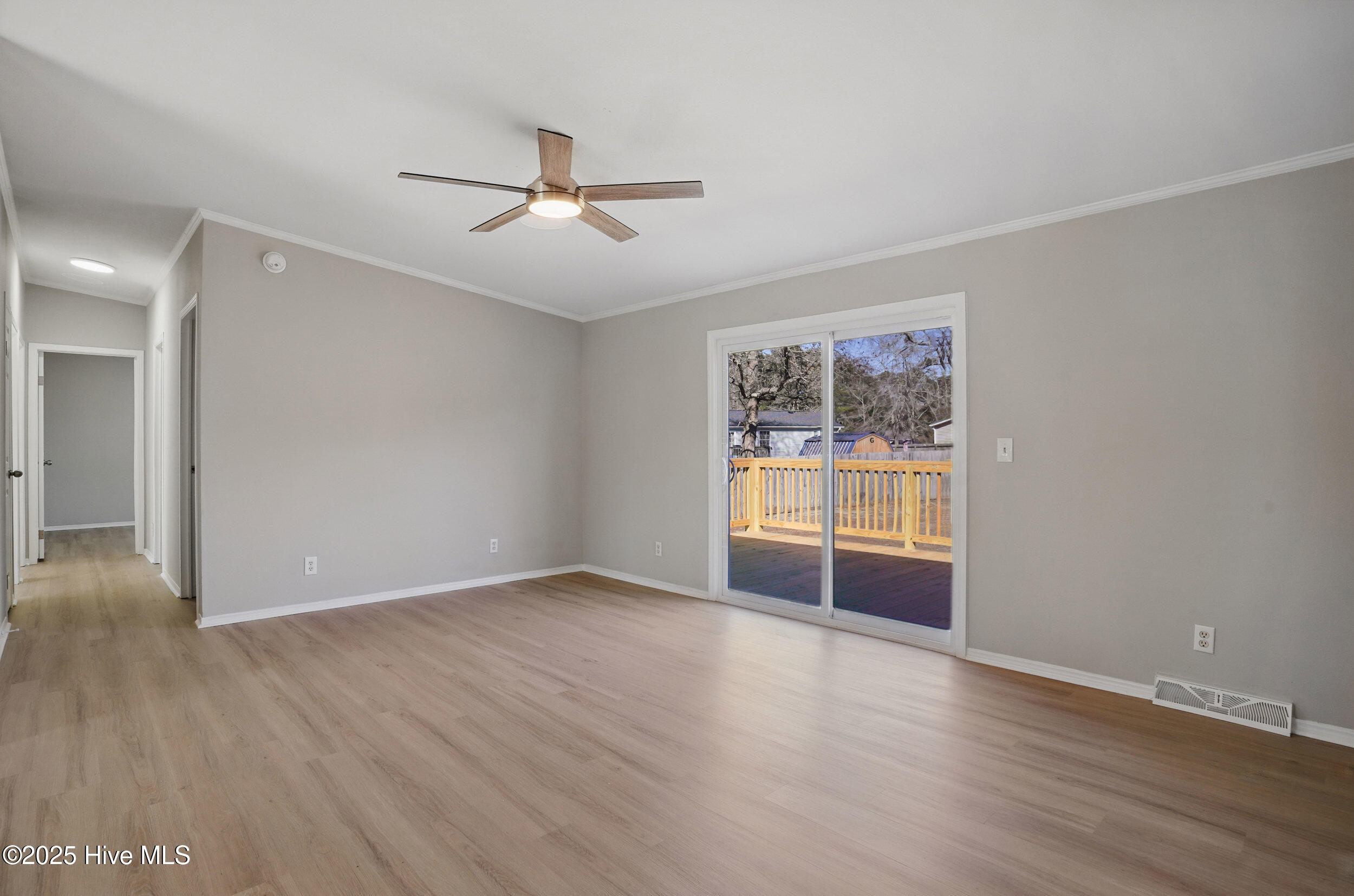 Vacant living room with light wood-look flooring, ceiling fan, and sliding glass doors to a deck.