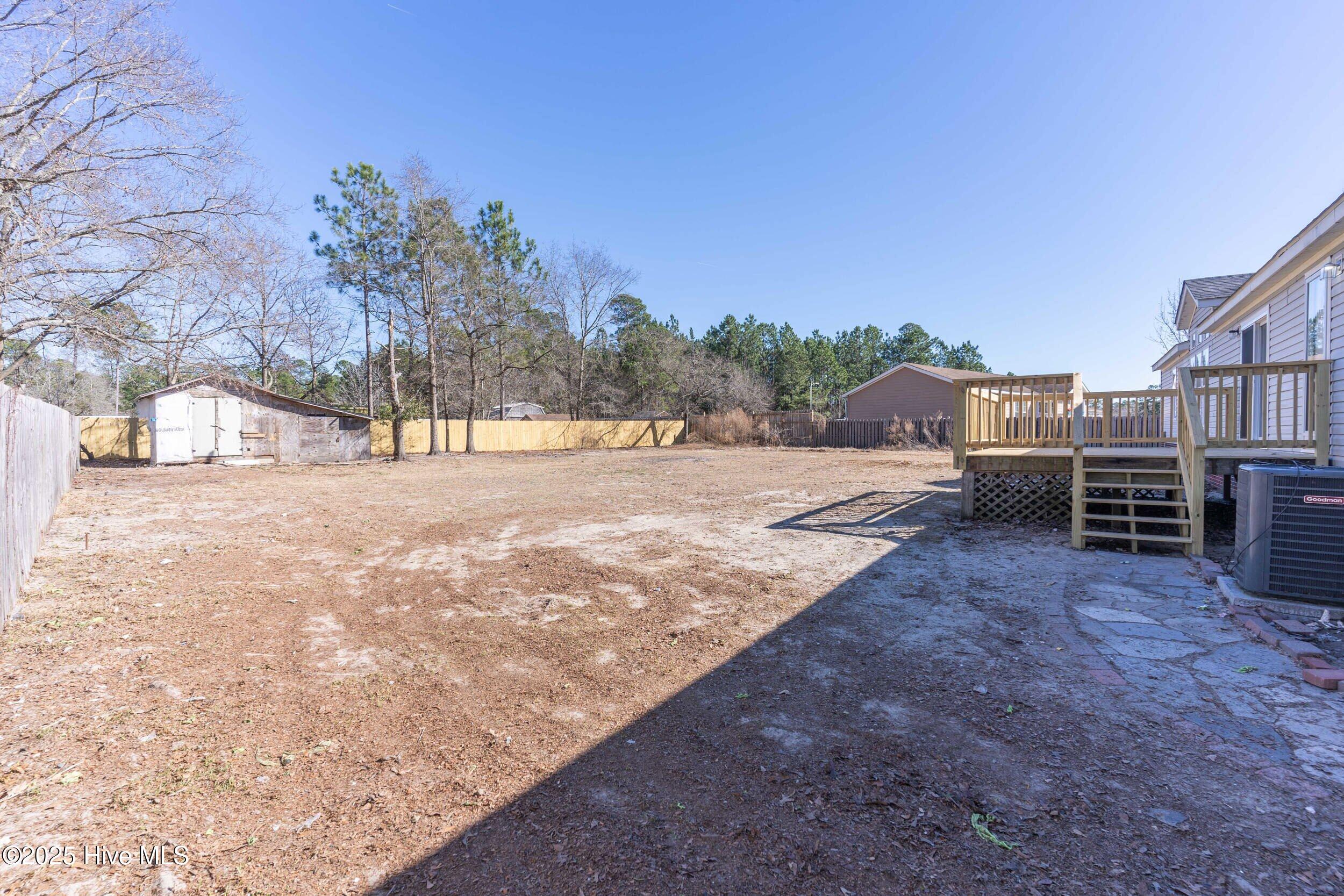 Backyard with a wooden deck, storage sheds, and a mostly bare yard.
