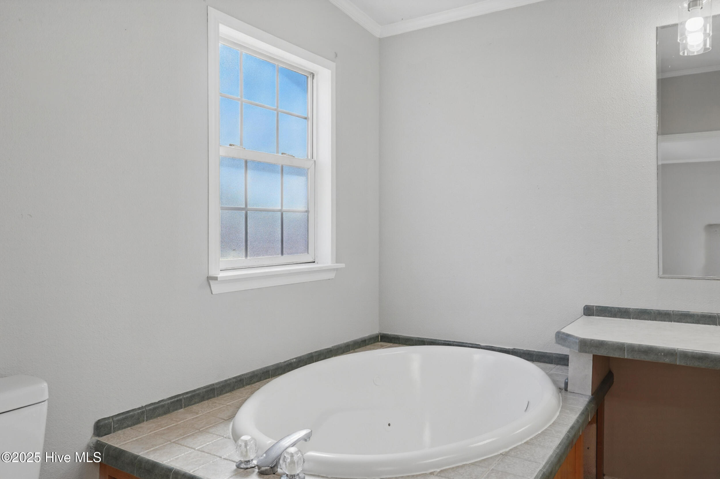 Bathroom with an oval built-in tub beneath a divided-pane window and tiled surround.