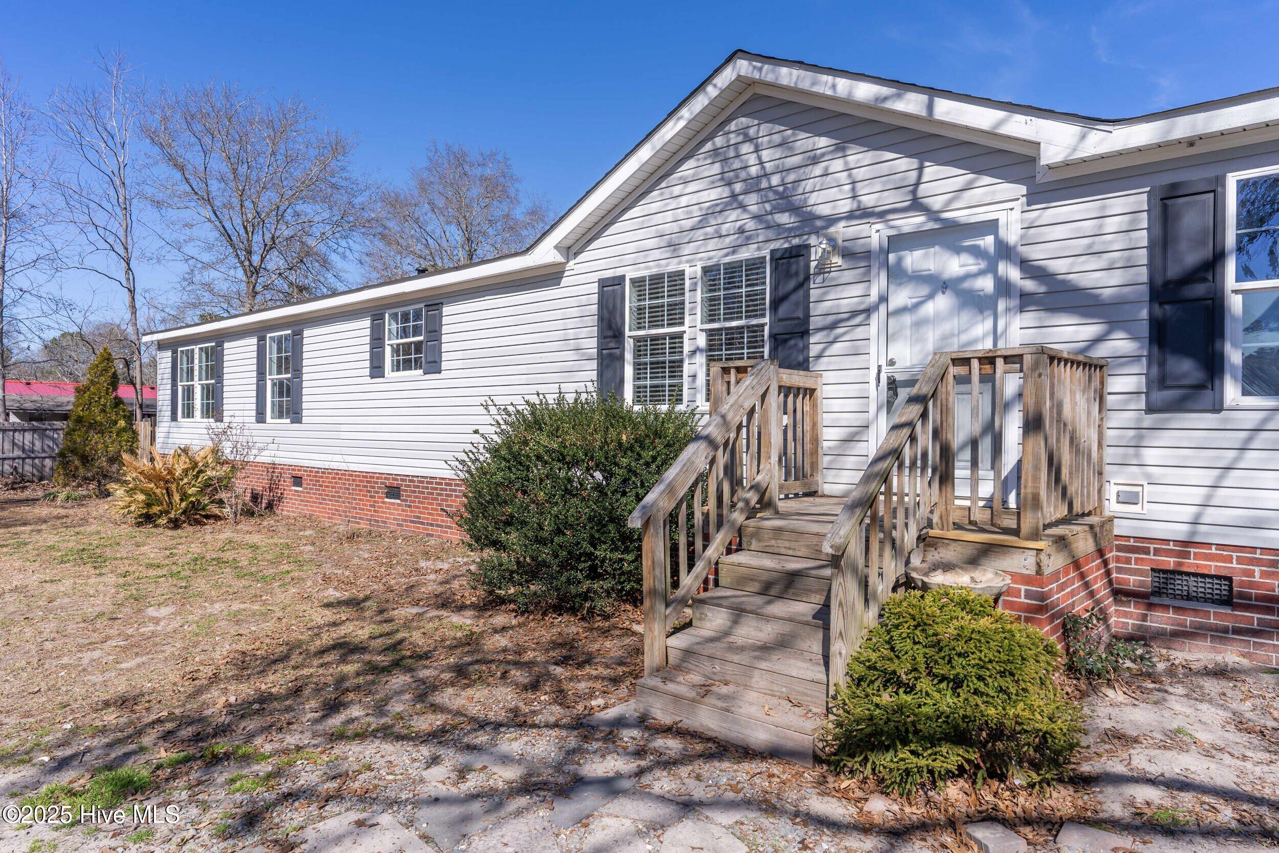 Single-story home with white siding, dark shutters, brick foundation, and wooden front steps.