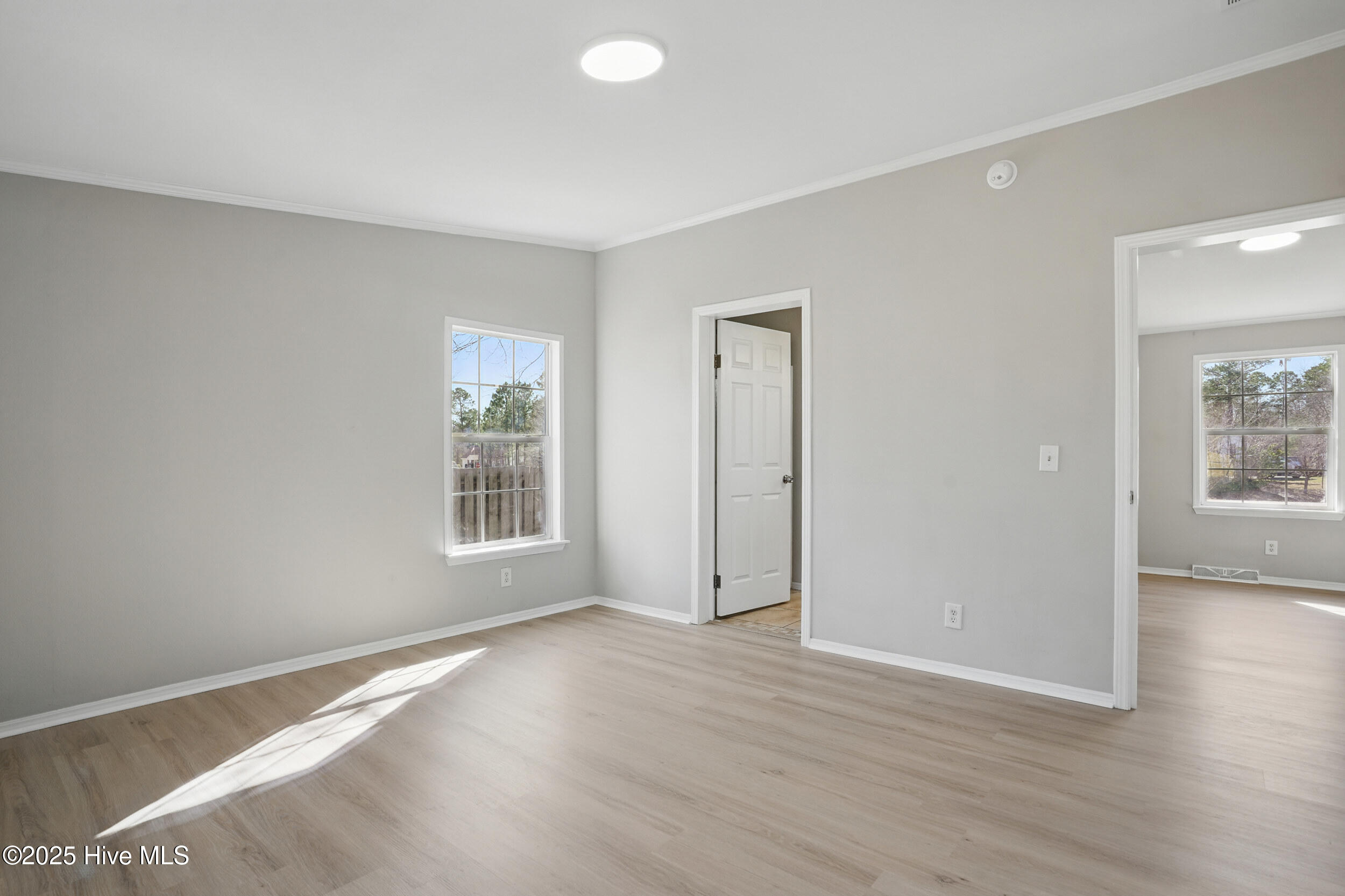 Empty room with light wood-look flooring, a window, and sunlight across the floor.