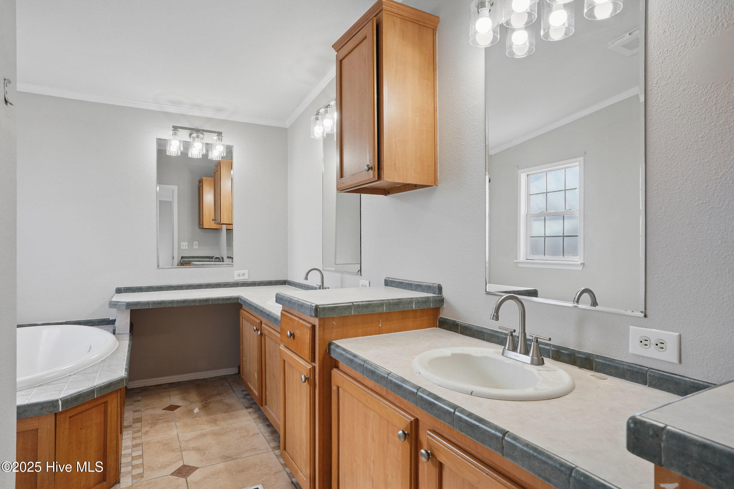 Bathroom with dual sinks, wood cabinets, large mirrors, and a partially visible soaking tub.