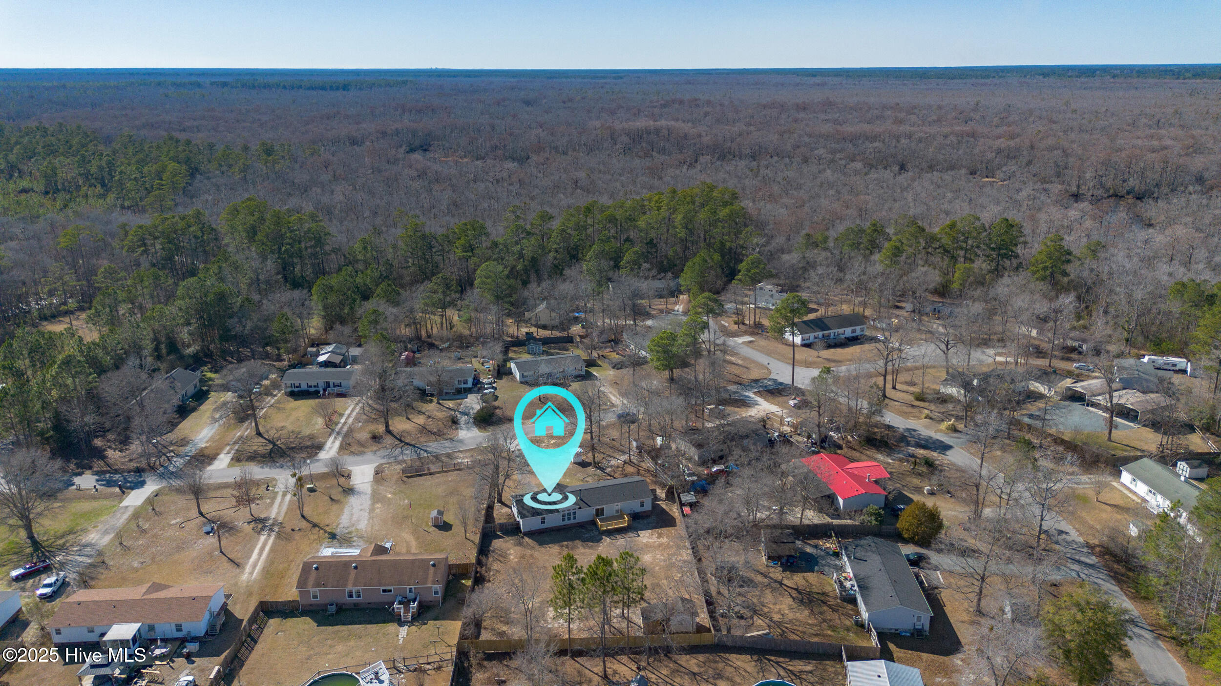 Aerial view of a single-story home among wooded lots, marked by a turquoise location pin.