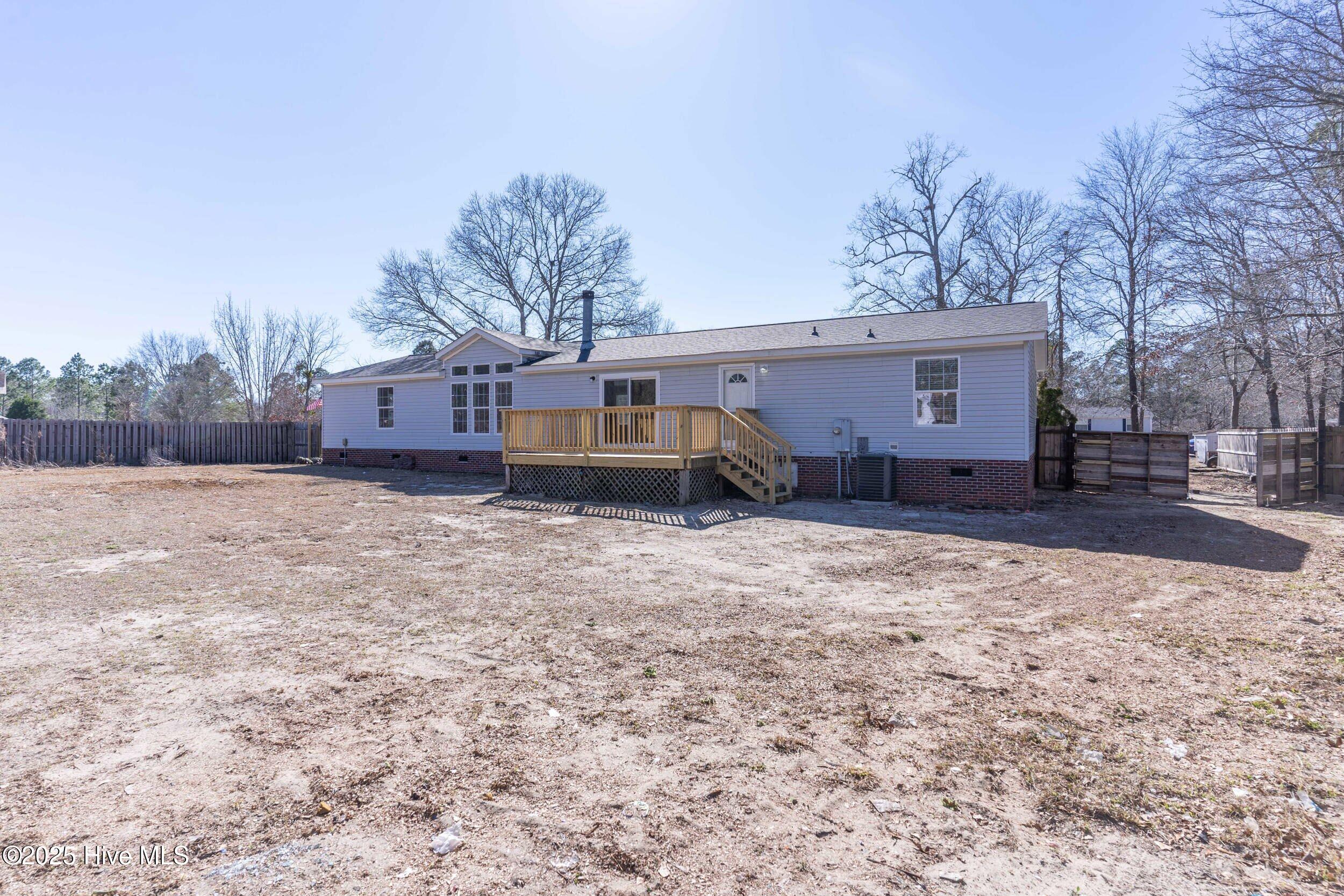Rear of a single-story home with a raised wooden deck and a fenced, mostly bare yard.