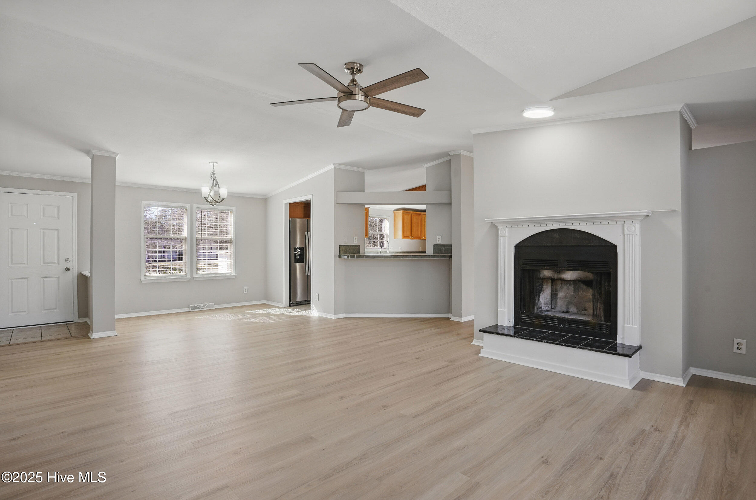 Open living room with light wood floors, a white-trimmed fireplace, and kitchen pass-through.