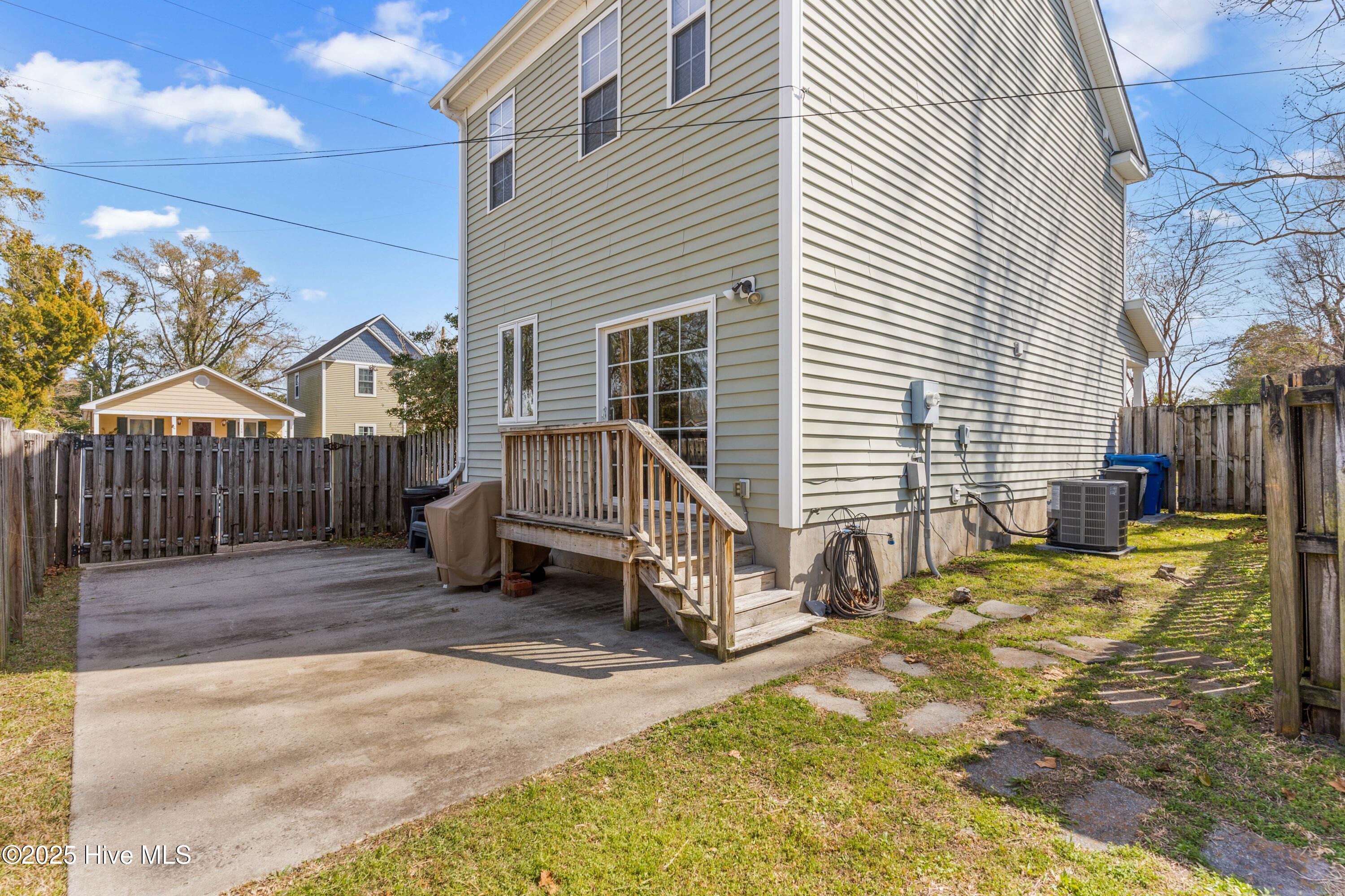 Two-story home’s fenced backyard with a wooden deck, concrete patio, and outdoor air-conditioning unit.