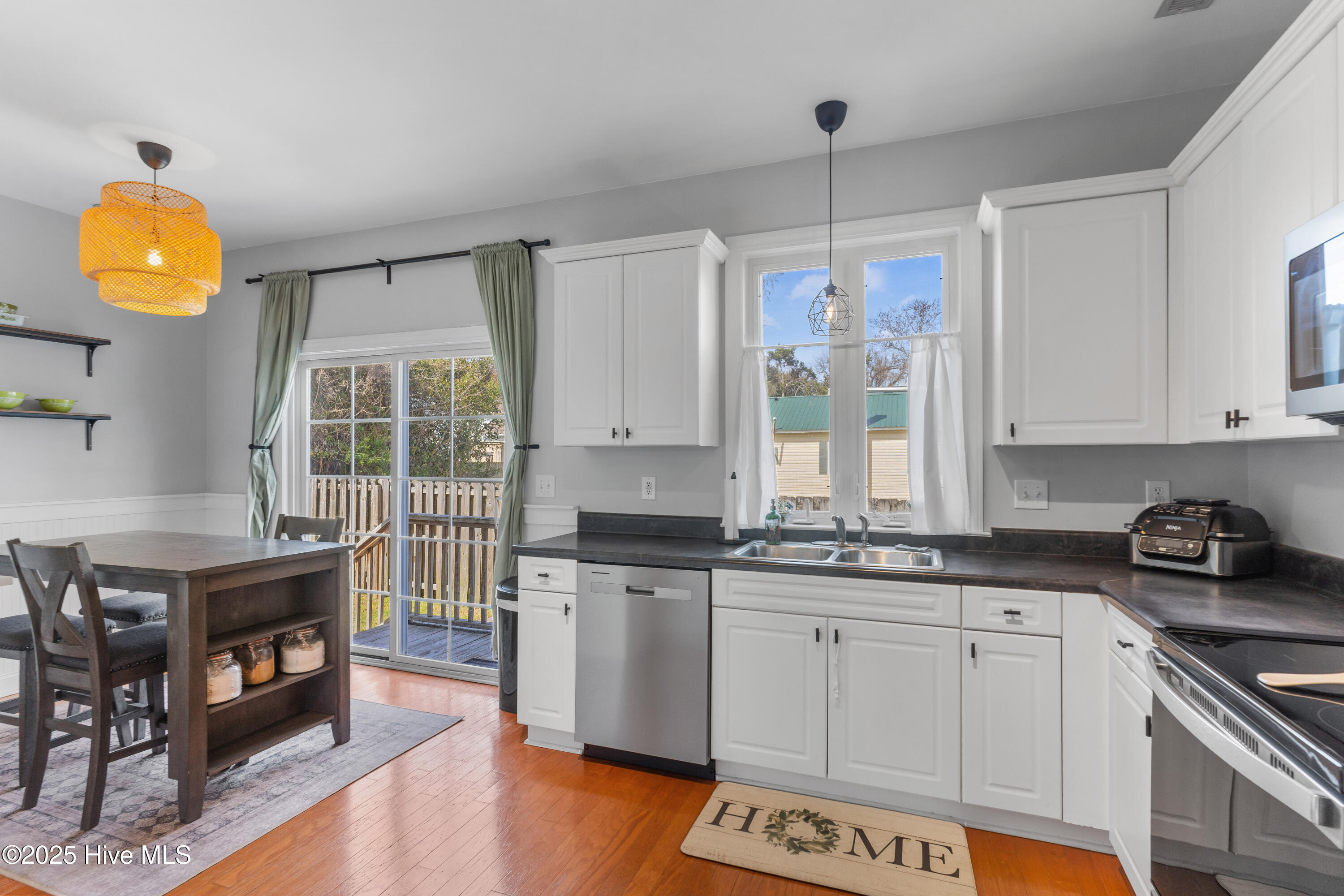 Kitchen with white cabinets, dark counters, stainless appliances, and an adjoining dining area beside a deck.